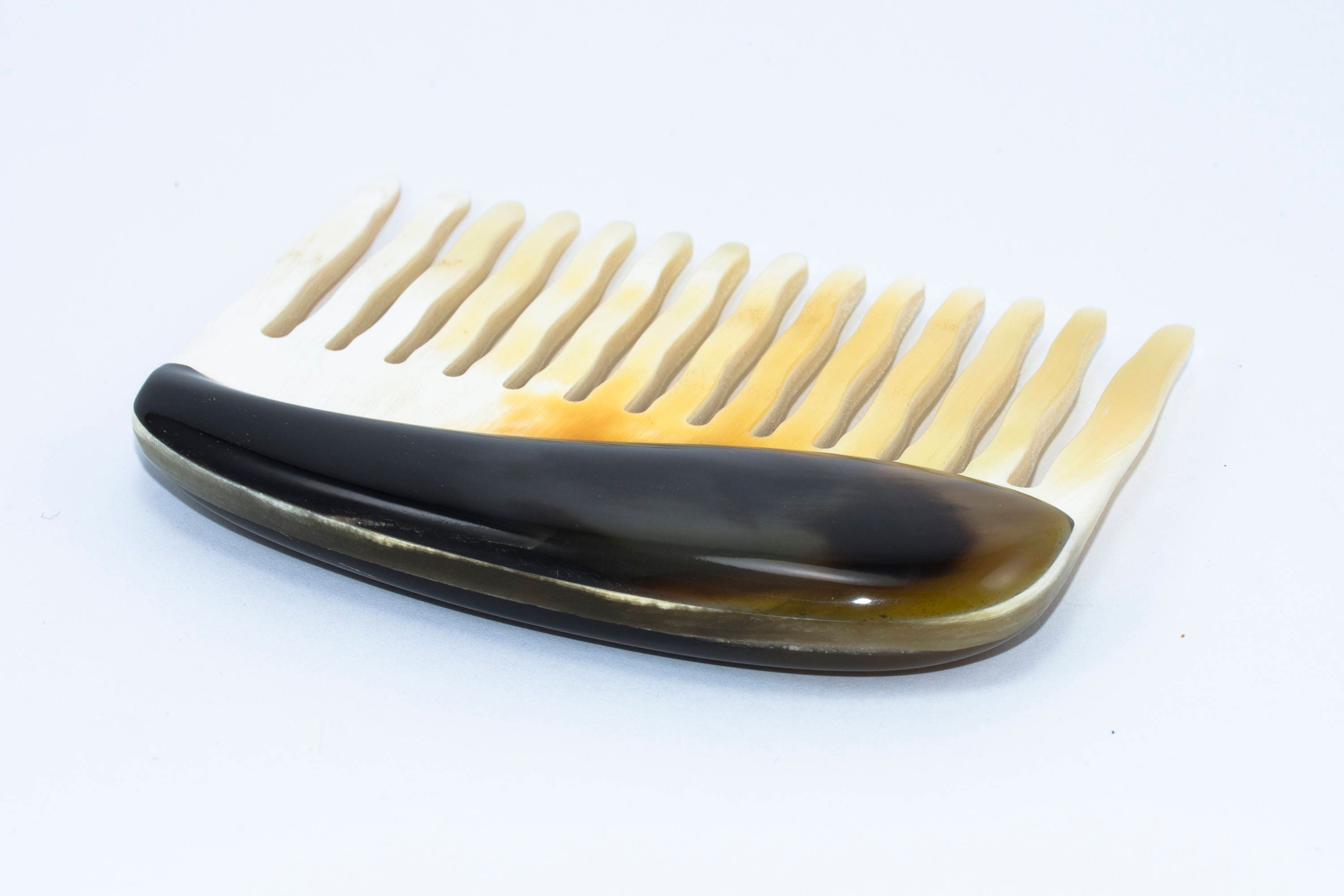 A beautifully crafted Buffalo Horn Comb with rounded teeth, showcasing its unique natural patterns and polished finish.