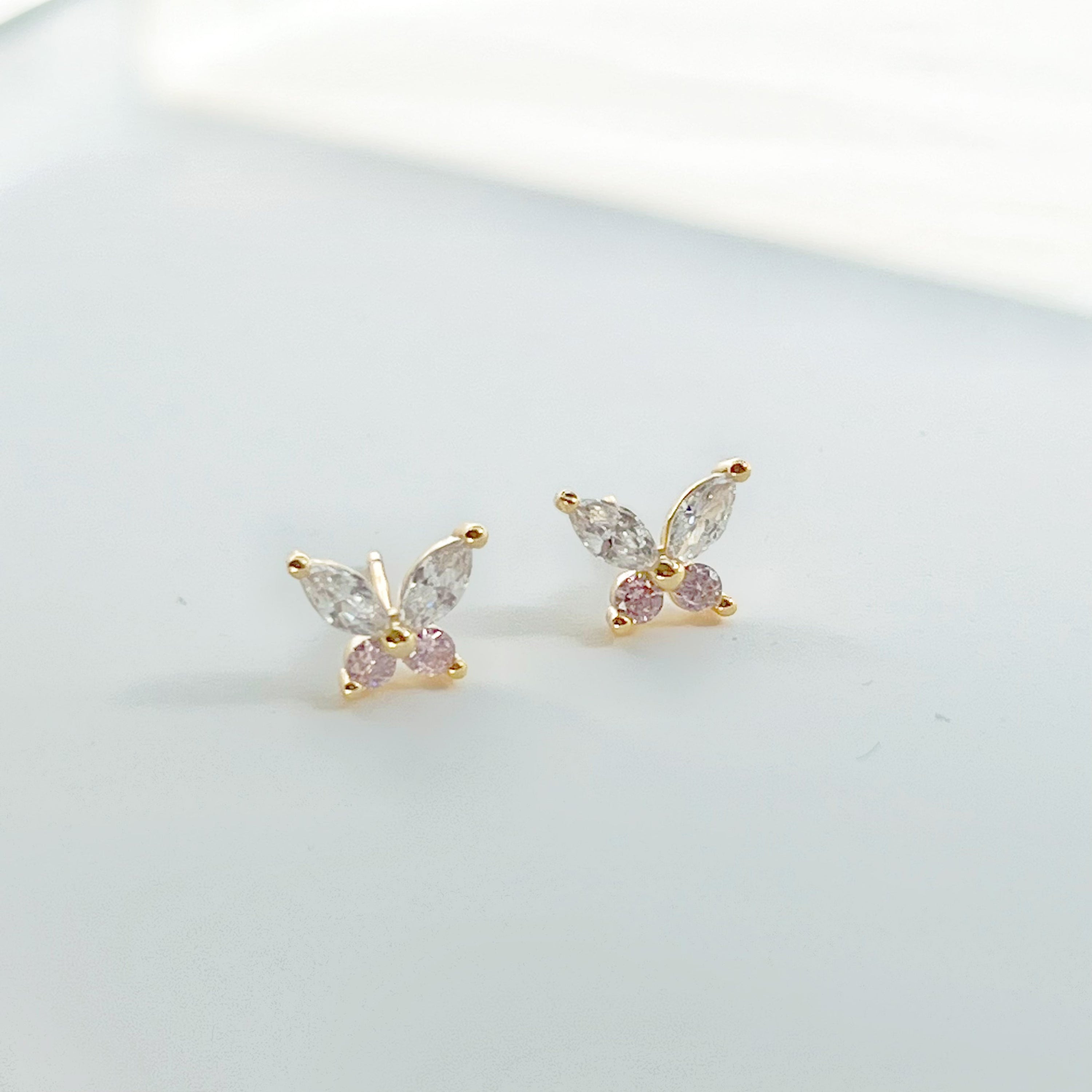 A pair of elegant butterfly gold stud earrings adorned with clear and pink zircon crystals, showcasing their delicate design.