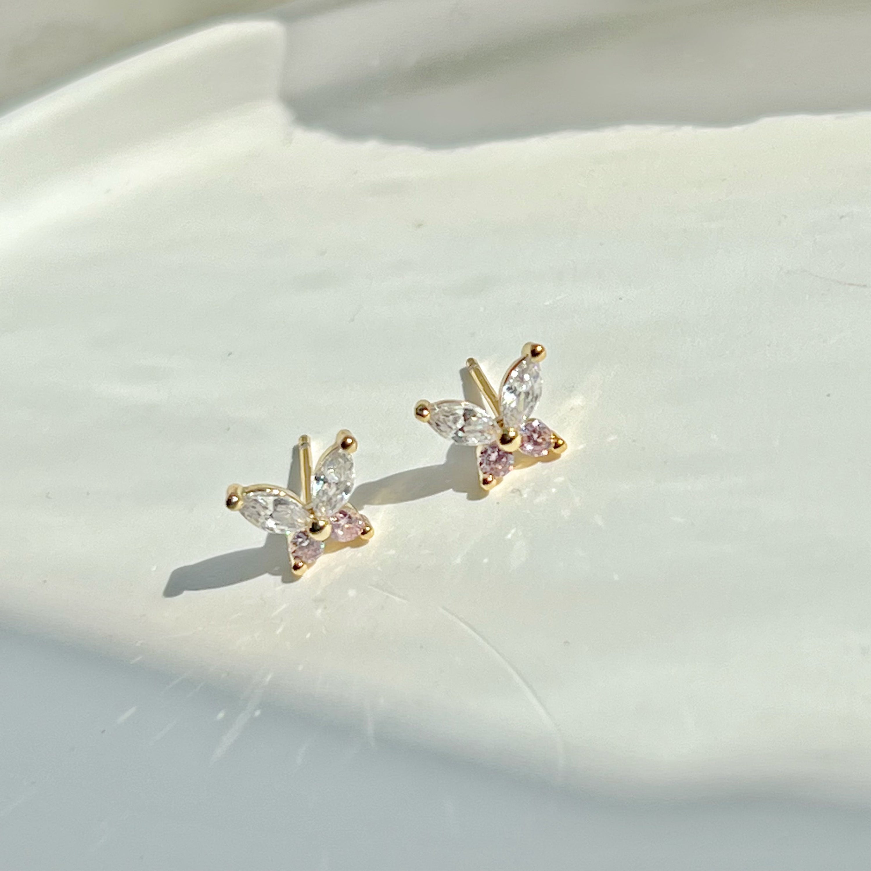 A pair of elegant butterfly gold stud earrings adorned with clear and pink zircon crystals, showcasing their delicate design.