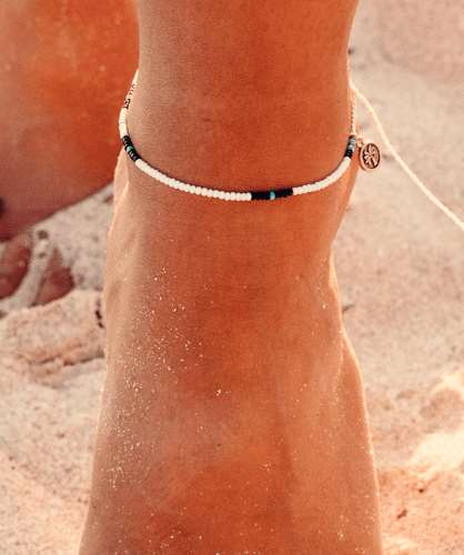 A vibrant handmade Cali Surf Anklet in white featuring multi-colored beads on a silk string, perfect for summer and beach activities.