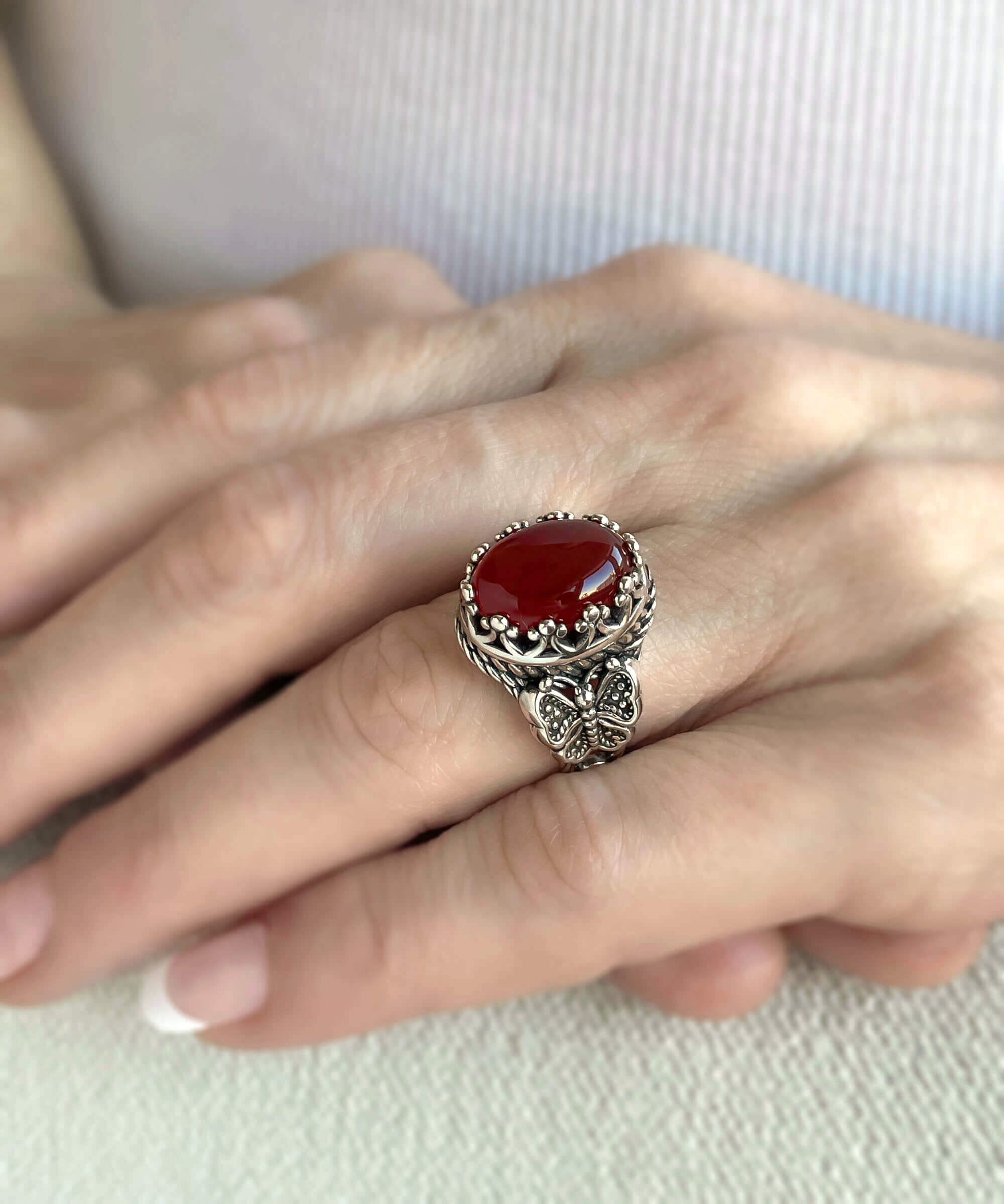 Elegant silver ring featuring intricate filigree butterfly design and a dark red carnelian gemstone.