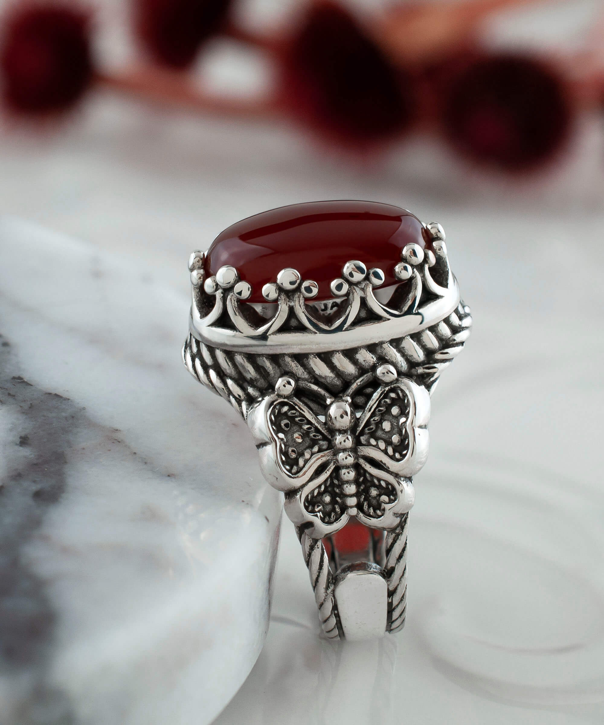 Elegant silver ring featuring intricate filigree butterfly design and a dark red carnelian gemstone.