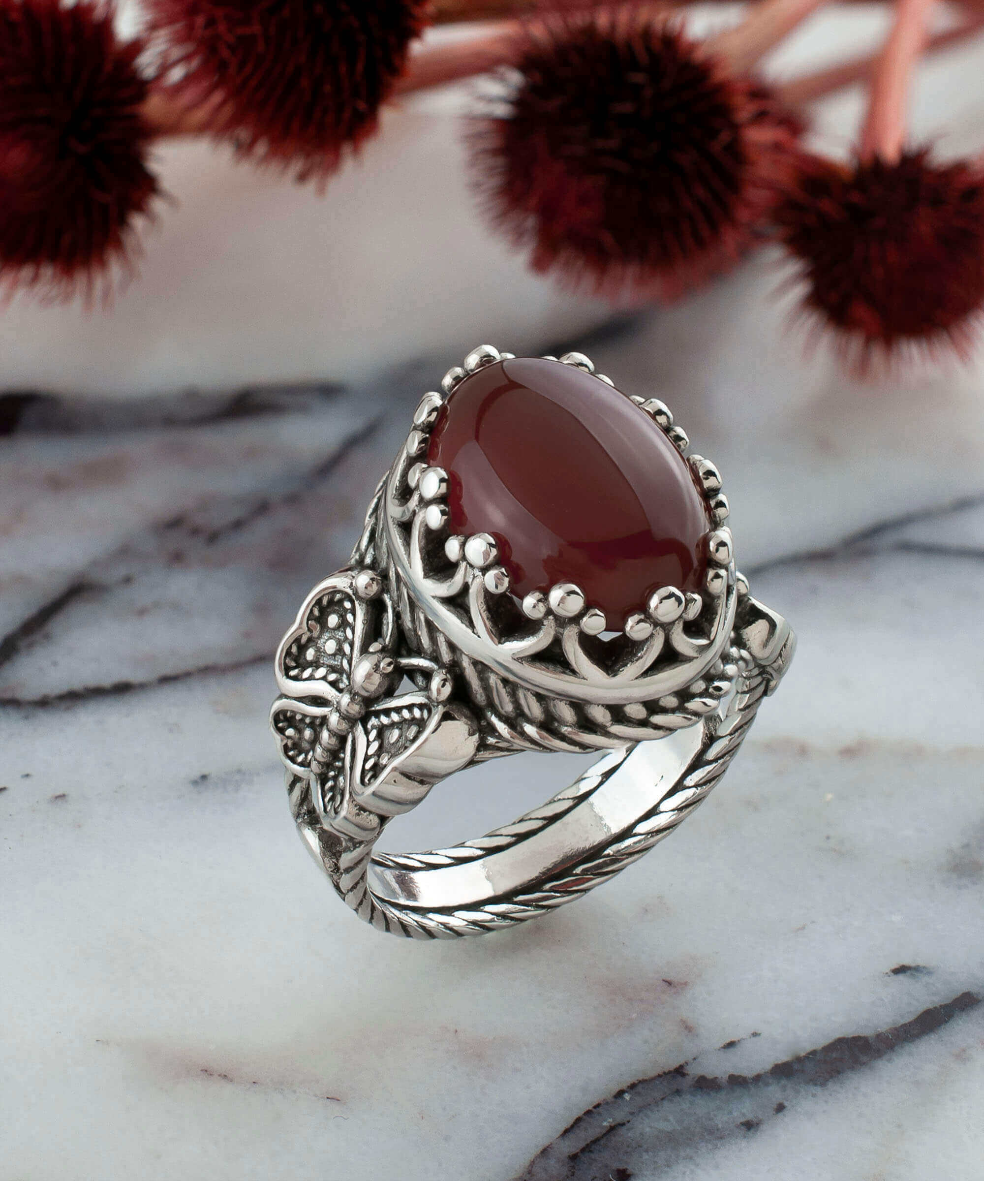 Elegant silver ring featuring intricate filigree butterfly design and a dark red carnelian gemstone.