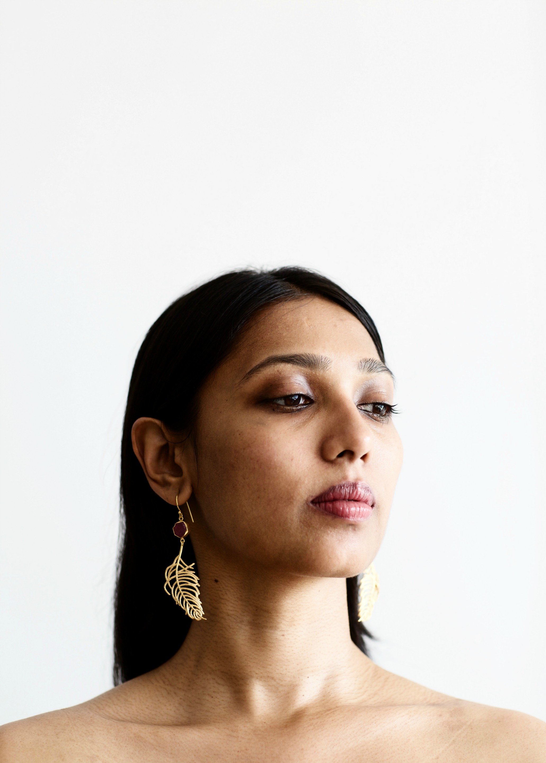 Elegant Cast Feather Earrings with 18K gold plating and clear quartz, showcasing a fluid feather design.