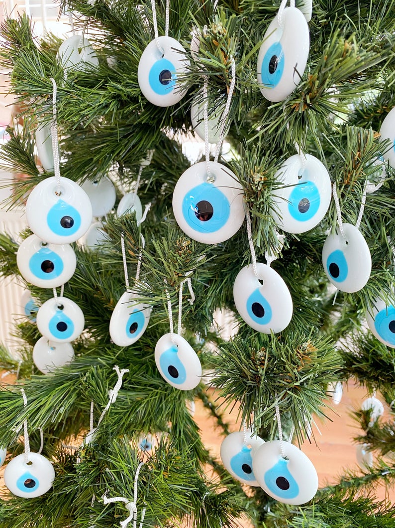 A collection of white evil eye bead Christmas tree ornaments made of glass, featuring intricate designs and hanging ropes for easy display.