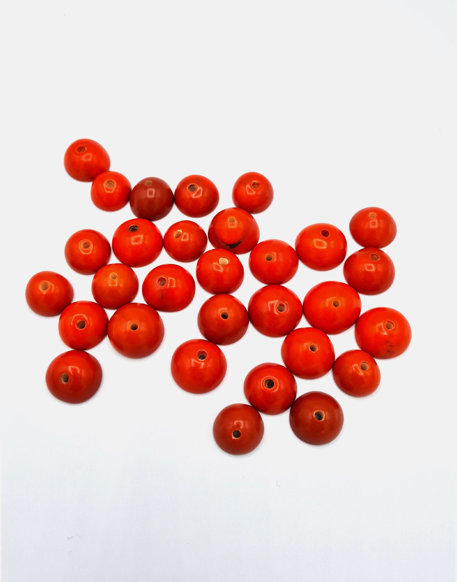 A collection of vibrant orange Tagua seeds, drilled and ready for crafting projects.