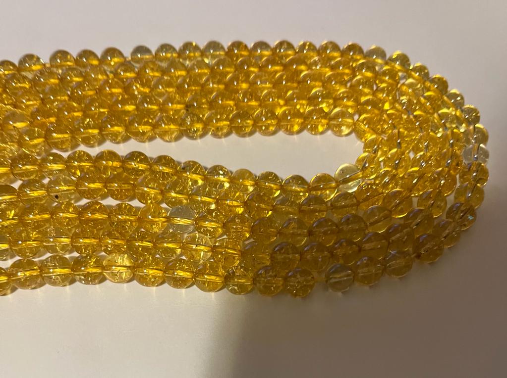 A strand of 8 mm round citrine natural gemstone beads, showcasing their vibrant yellow color and unique natural variations.