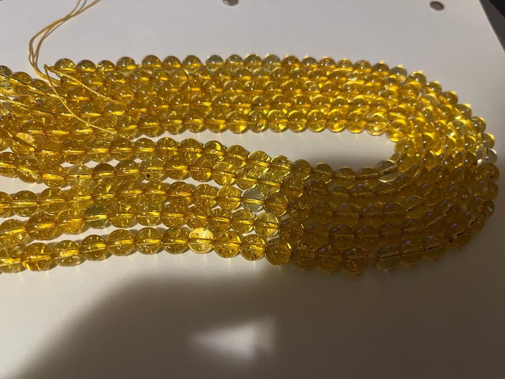 A strand of 8 mm round citrine natural gemstone beads, showcasing their vibrant yellow color and unique natural variations.