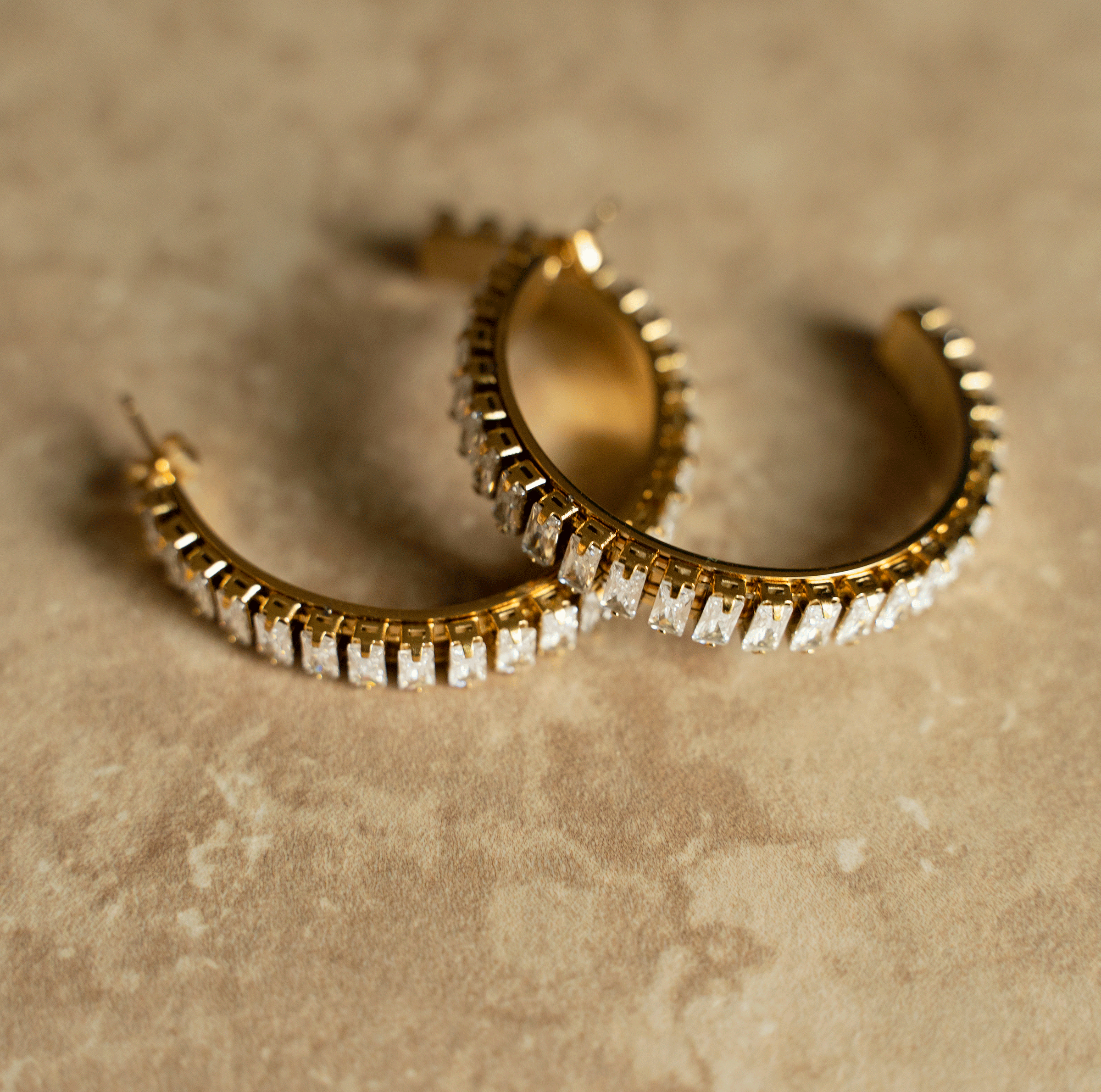 Elegant CLARE Hoops made of stainless steel with 18k gold plating and baguette cut stones, showcasing contemporary design.