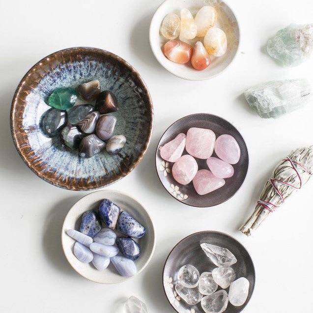 A serene consultation setting with various colorful crystals, sage leaves, and an aluminum tin for crystal storage.