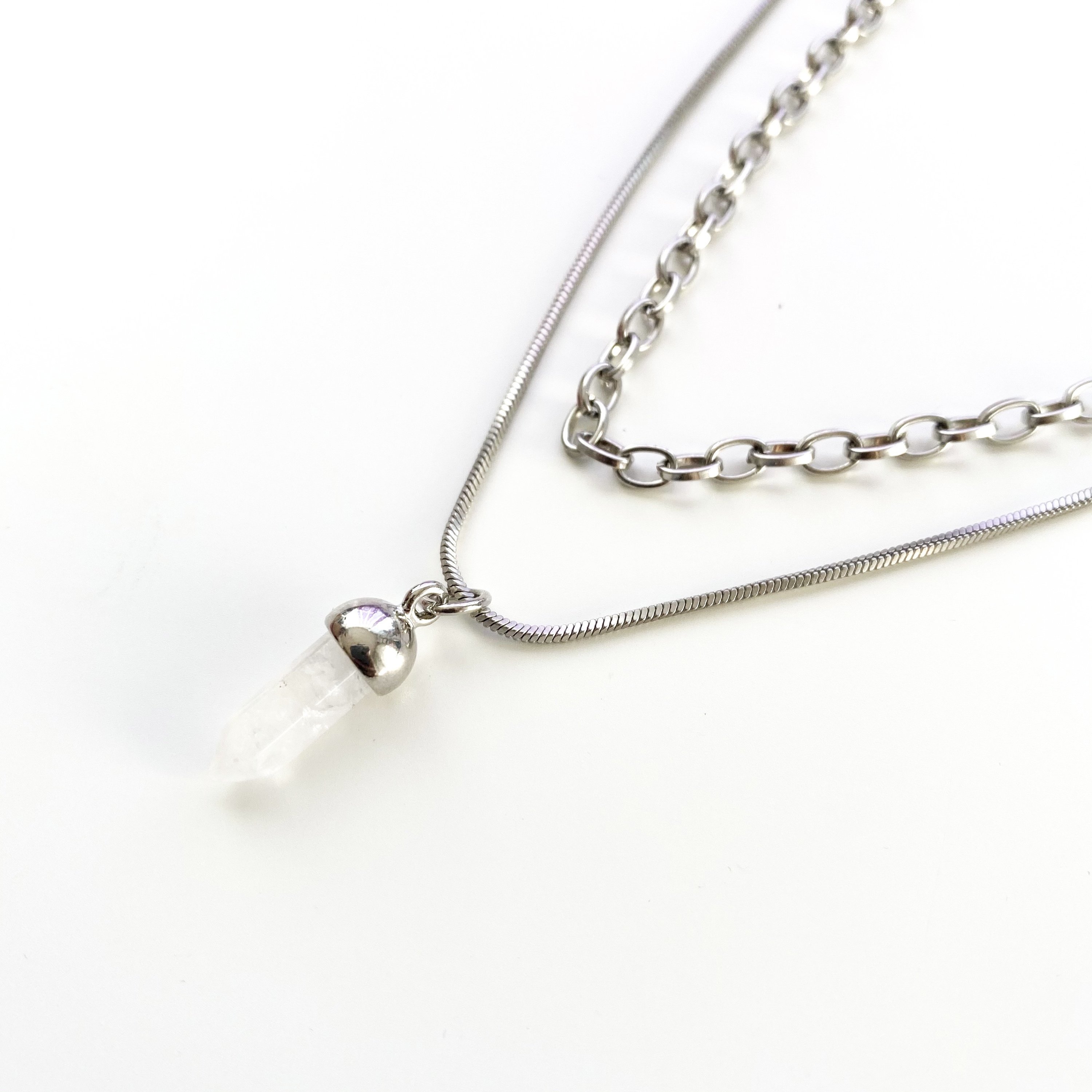 A stylish triple strand necklace in silver tones featuring a clear quartz point charm, elegantly displayed on a soft background.