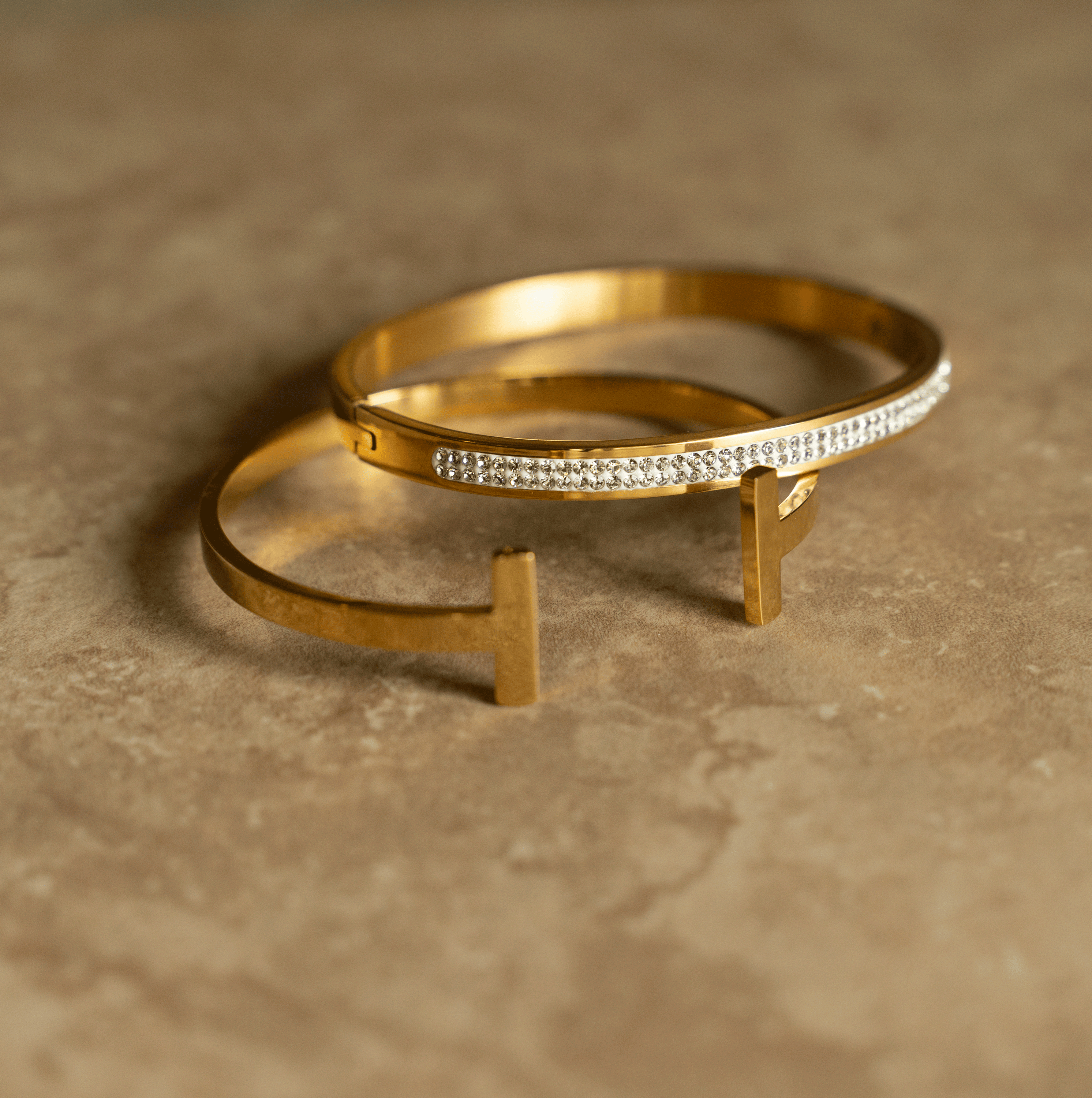 The CLEO Cuff is a stylish open bangle with a geometric 'T' shaped top, featuring 18K gold plating over stainless steel.