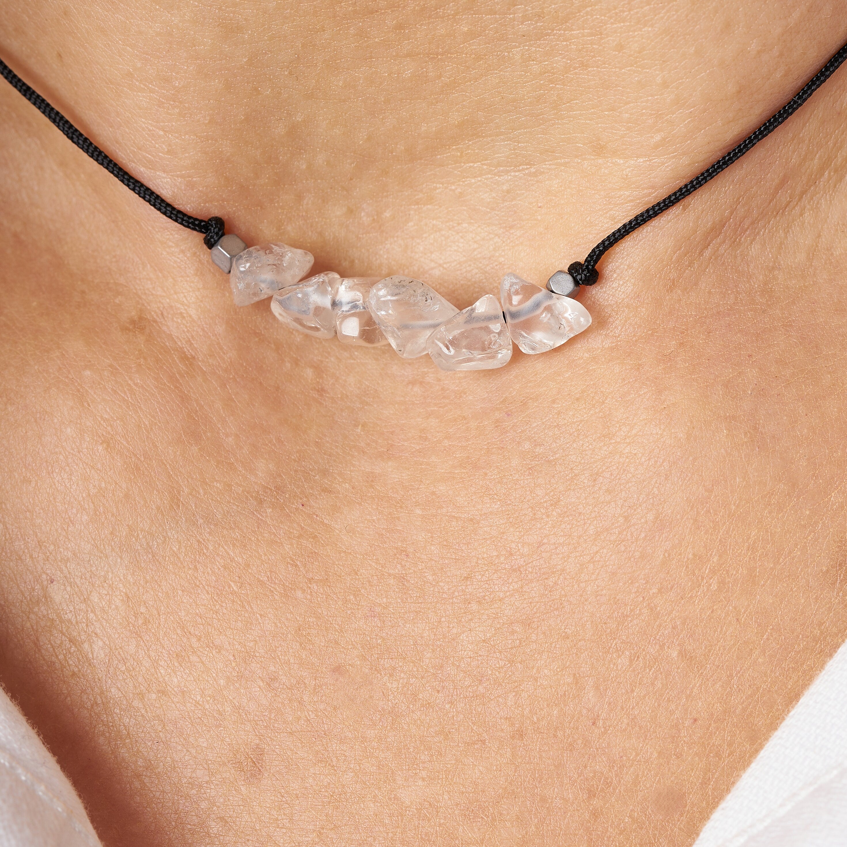 Collar de cuarzo transparente en bruto con seis piedras irregulares, atado a un cordón negro, presentado en una tarjeta de regalo.