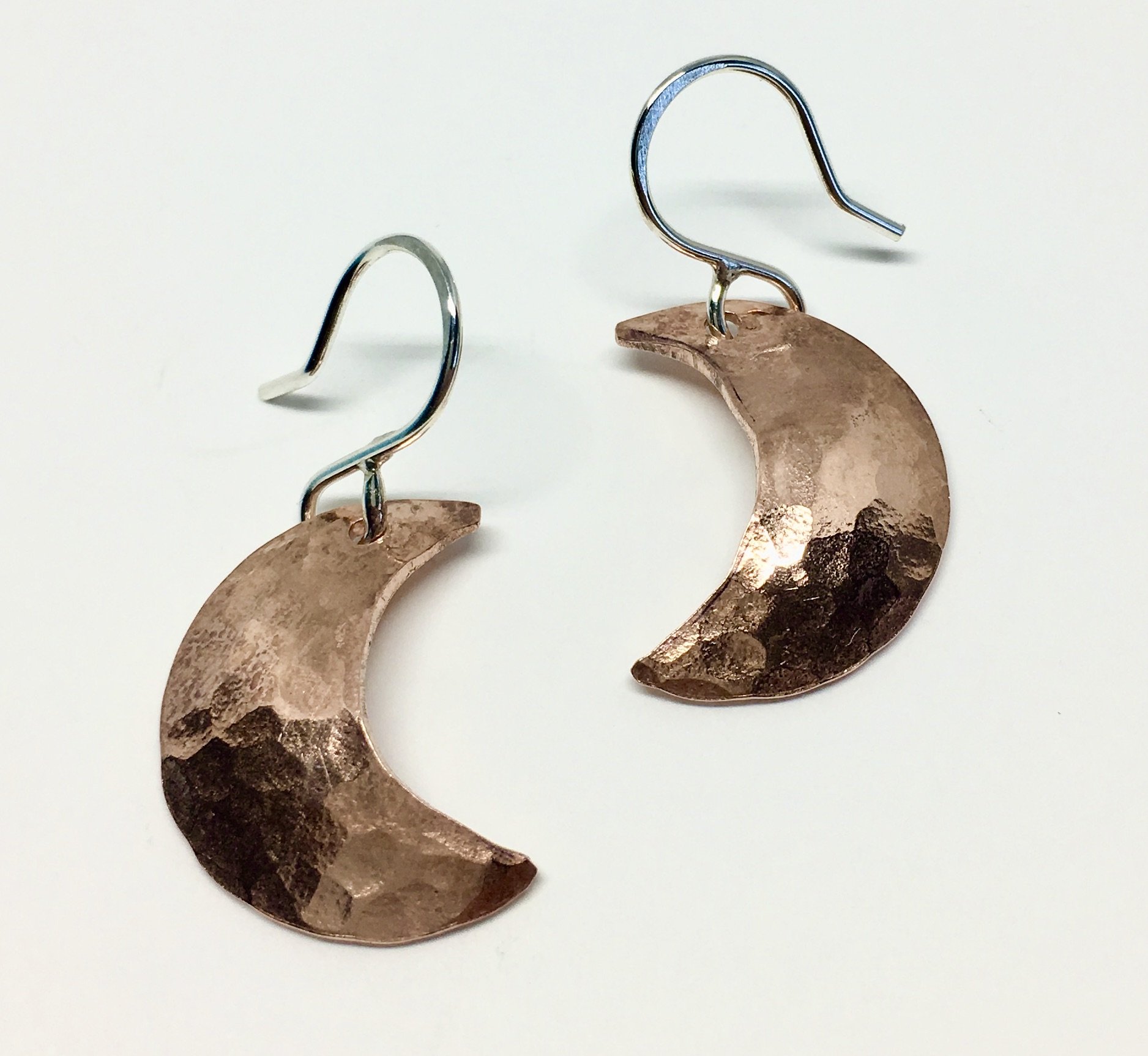 A pair of Crescent Moon Earrings featuring domed discs with a hammered texture, hanging from handmade sterling silver ear wires.