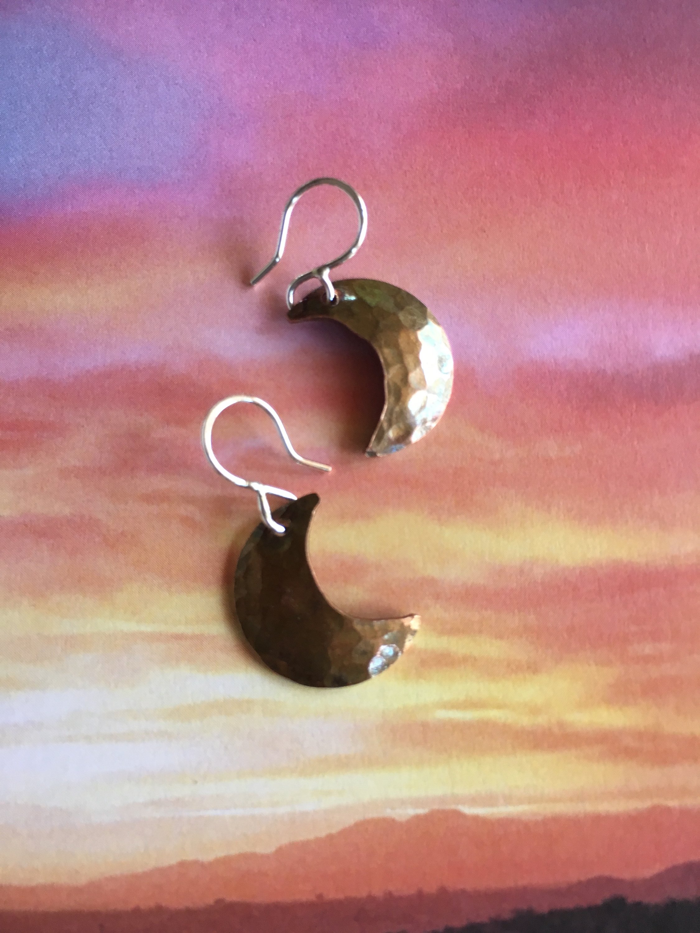 A pair of Crescent Moon Earrings featuring domed discs with a hammered texture, hanging from handmade sterling silver ear wires.