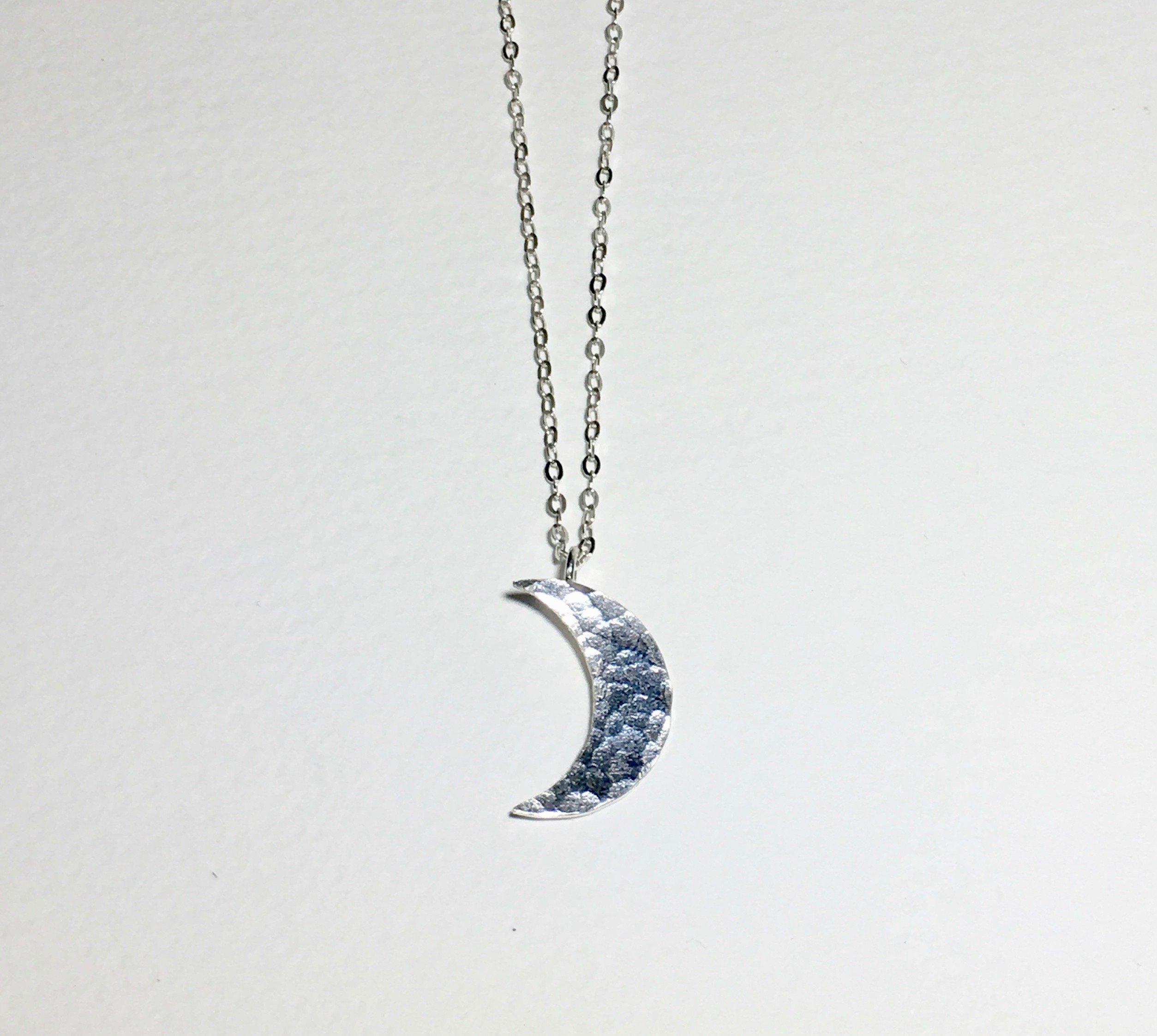 A beautifully handcrafted crescent moon necklace with a hammered texture, showcasing its unique design and sustainable materials.