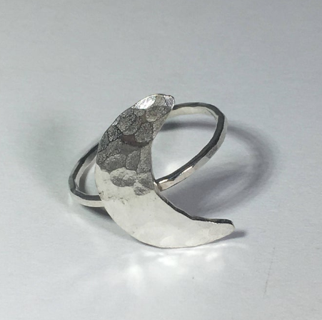 A handcrafted Crescent Moon Ring made from recycled metals, featuring a rustic design that mimics the moon's surface.