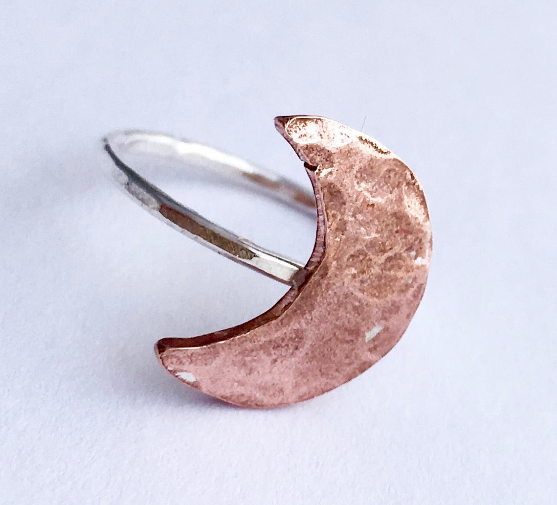 A handcrafted Crescent Moon Ring made from recycled metals, featuring a rustic design that mimics the moon's surface.