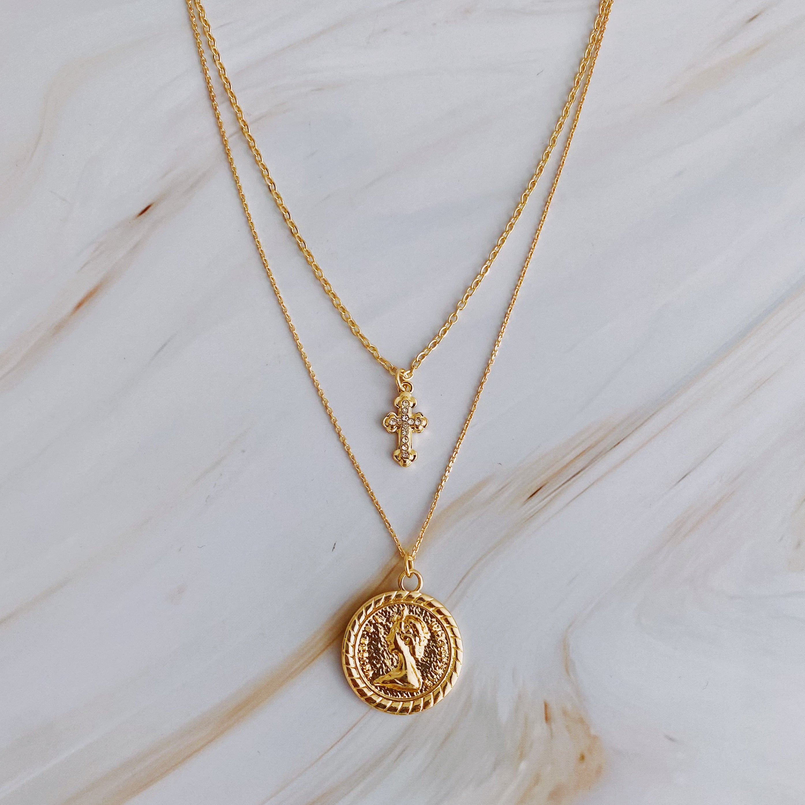 Cross and Coin Layered Necklace featuring a gold plated cross and classic coin design, elegantly layered for a stylish look.