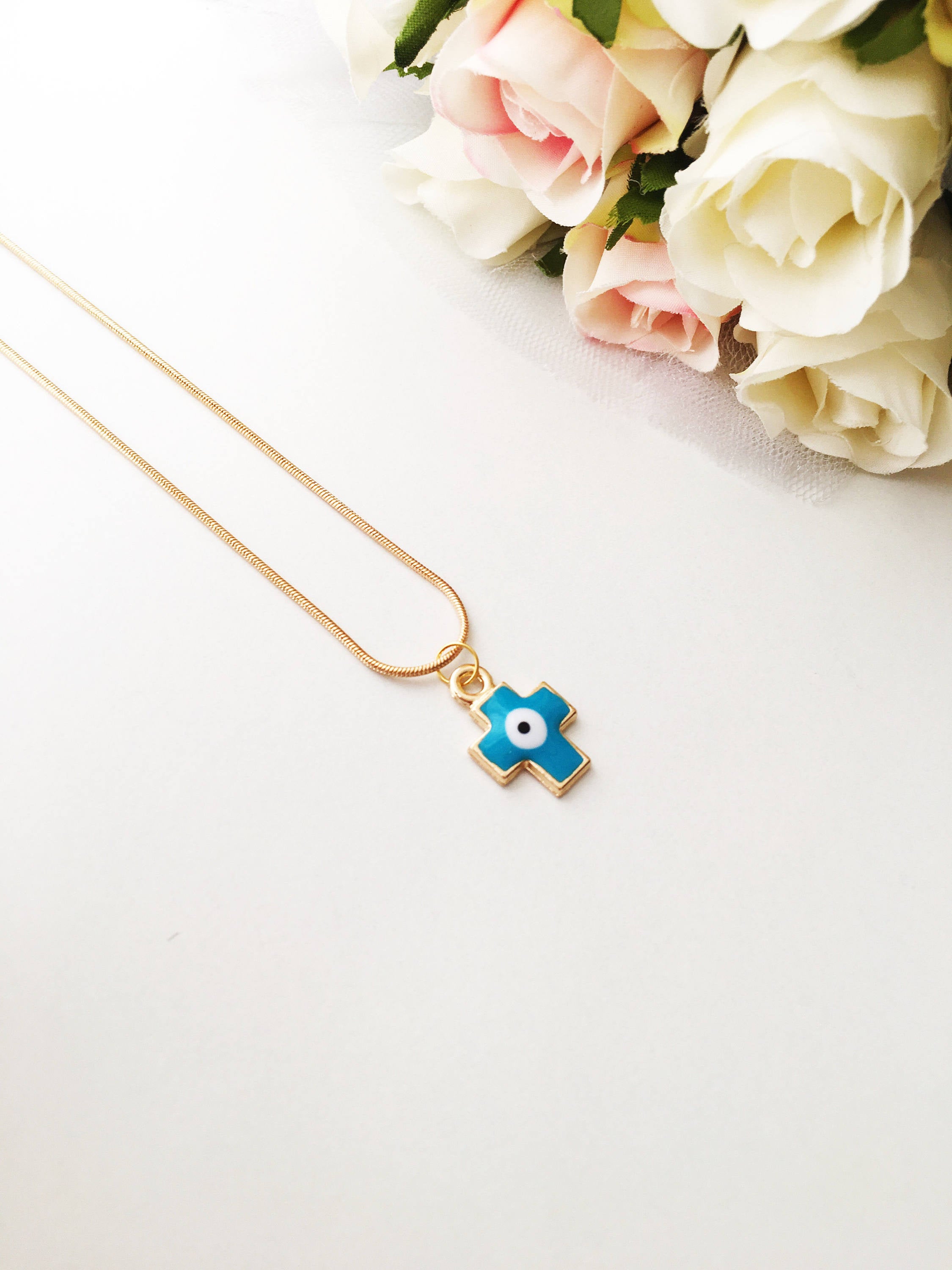 Handmade Cross Evil Eye Necklace featuring blue and red charm on a gold plated chain, symbolizing protection and spirituality.