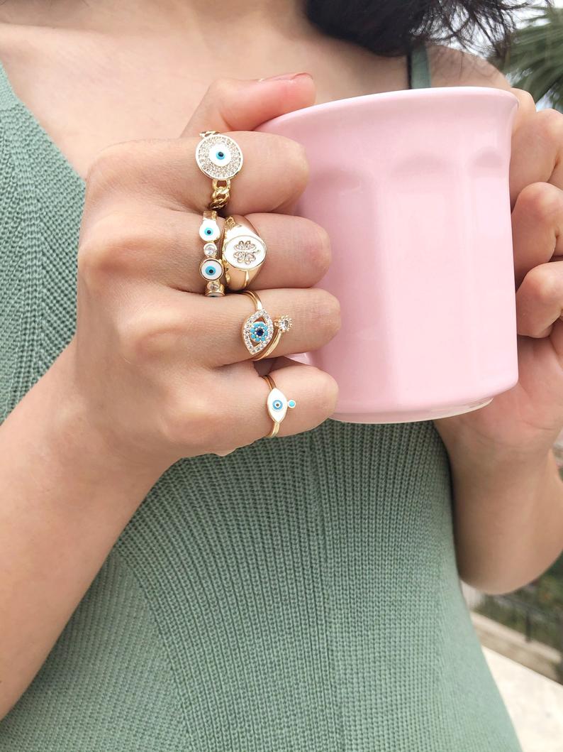 A collection of dainty adjustable evil eye rings in gold, featuring a white evil eye design, perfect for everyday wear.