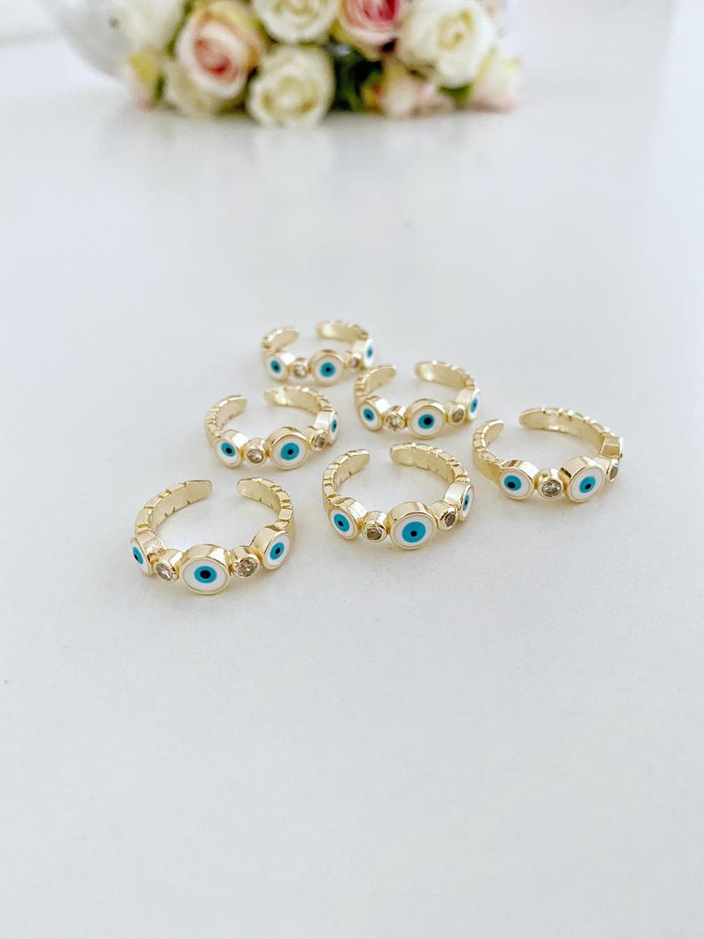 A collection of dainty adjustable evil eye rings in gold, featuring a white evil eye design, perfect for everyday wear.