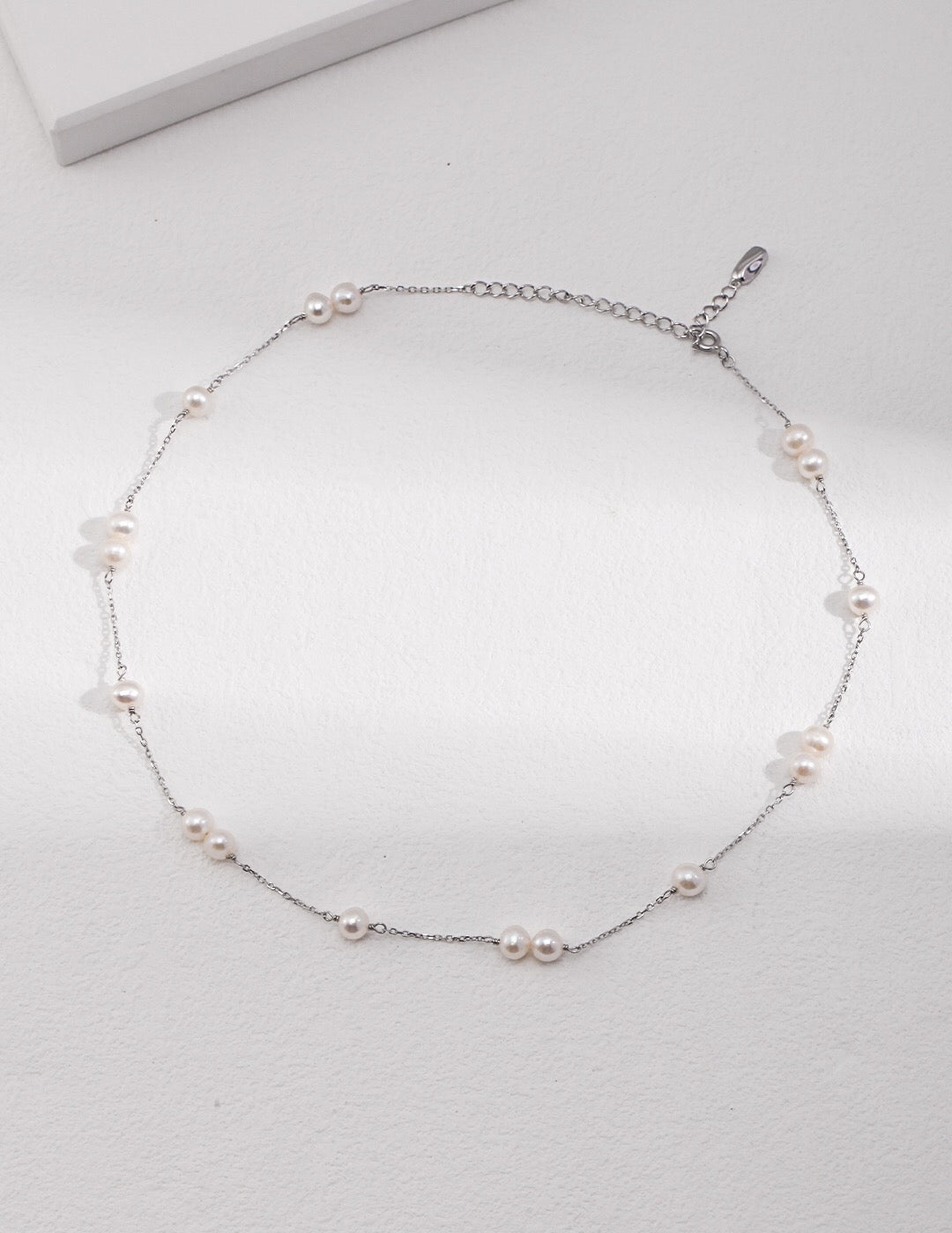 A delicate Dainty Freshwater Pearl Choker Necklace featuring genuine pearls and sterling silver, elegantly displayed on a soft fabric background.