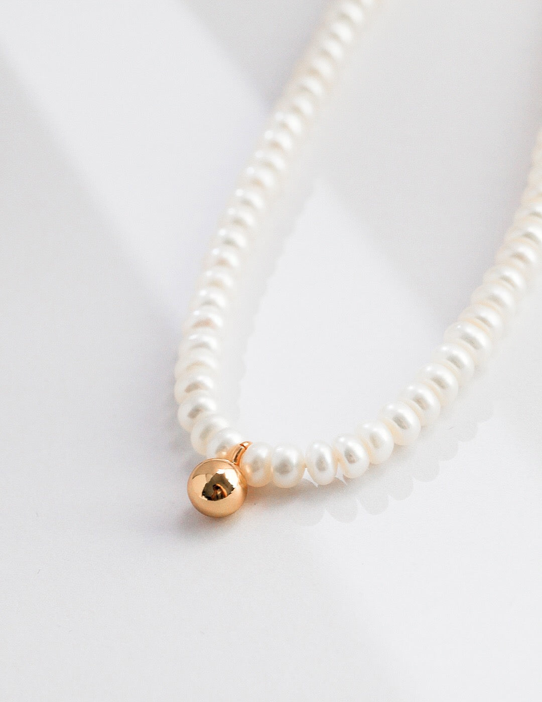 A delicate Dainty Pearl Beaded Necklace featuring natural pearls and gold vermeil, elegantly displayed on a soft fabric background.