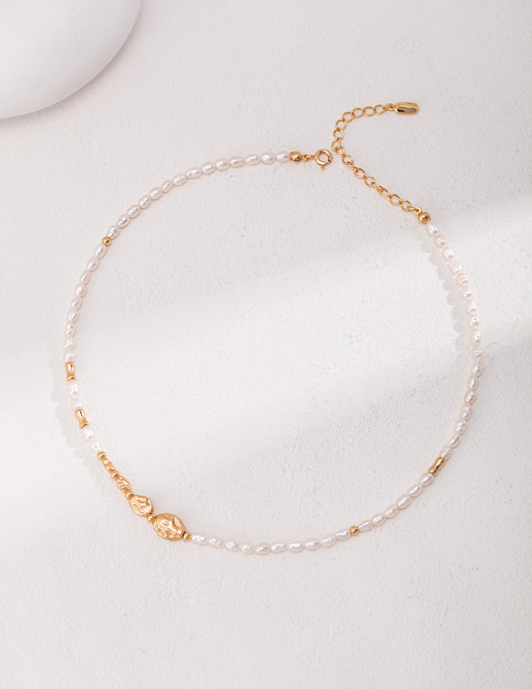 A delicate Dainty Rice Pearl Necklace featuring freshwater pearls and gold vermeil, elegantly displayed on a soft fabric background.