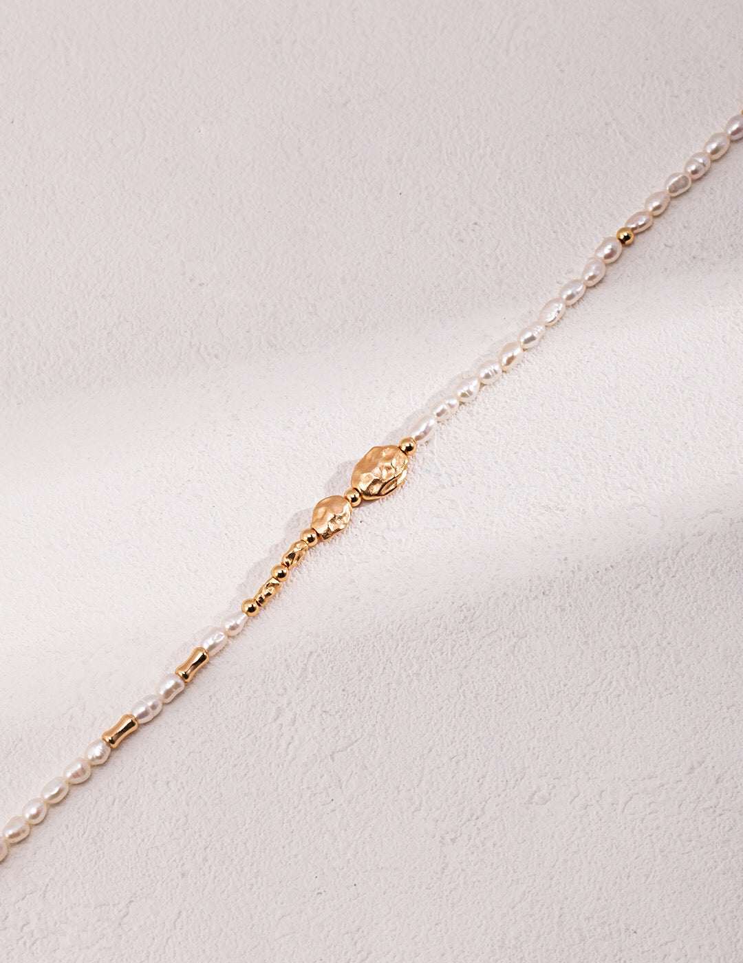 A delicate Dainty Rice Pearl Necklace featuring freshwater pearls and gold vermeil, elegantly displayed on a soft fabric background.