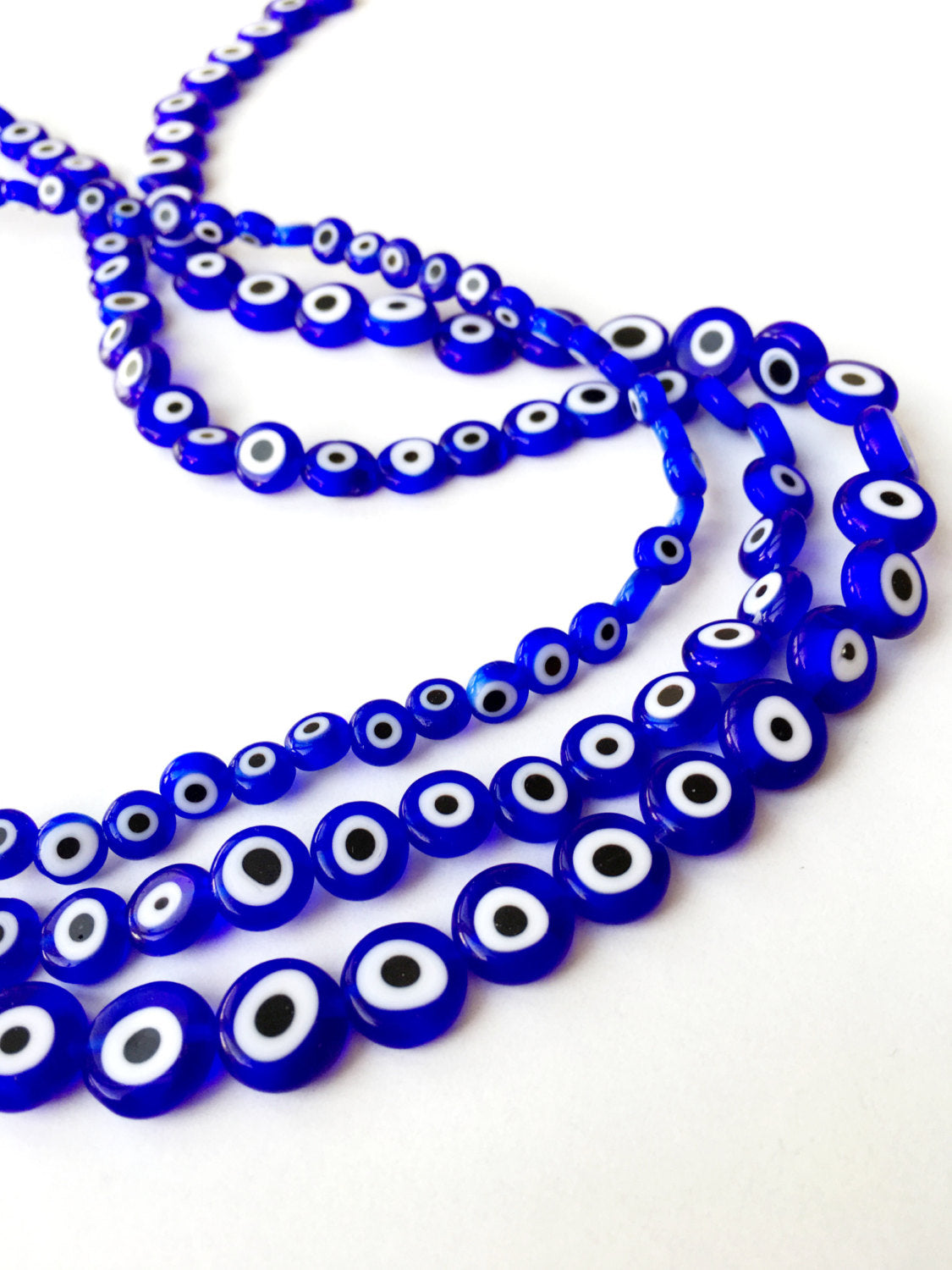 A collection of dark blue flat evil eye beads in various sizes, showcasing their unique handmade designs from Turkey.