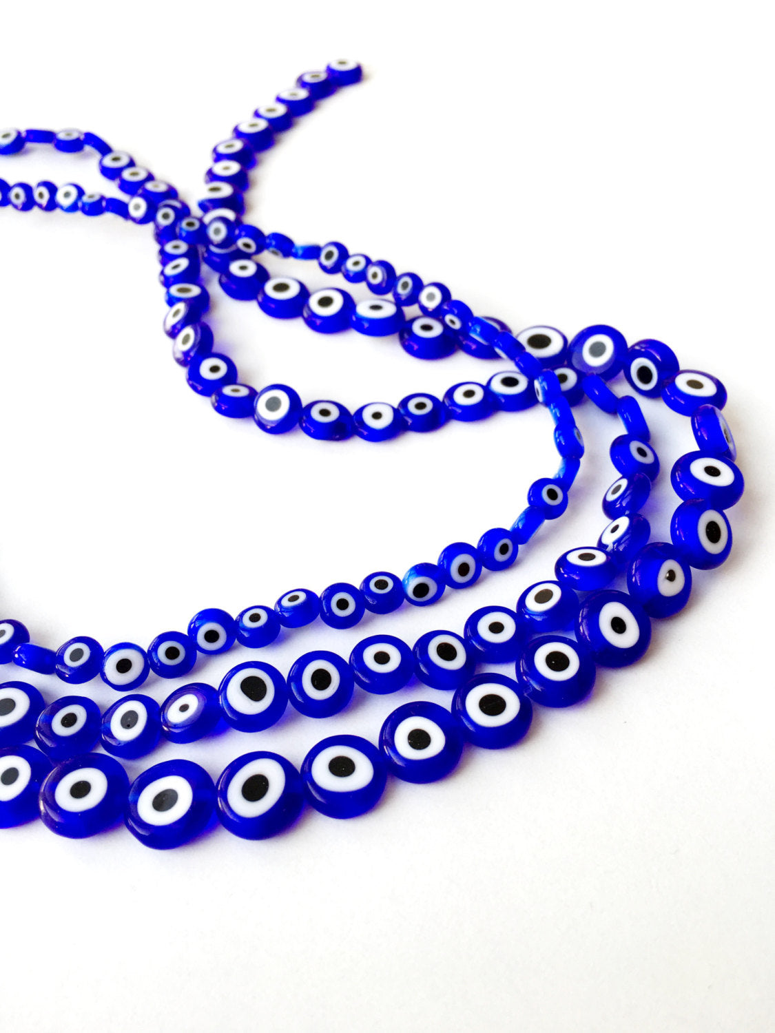 A collection of dark blue flat evil eye beads in various sizes, showcasing their unique handmade designs from Turkey.