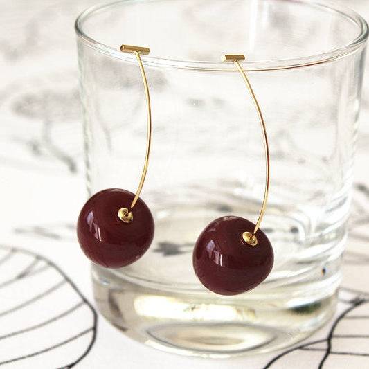 A pair of vintage rockabilly style dark red cherry earrings, featuring large resin cherries and gold-coated bronze ear wires.