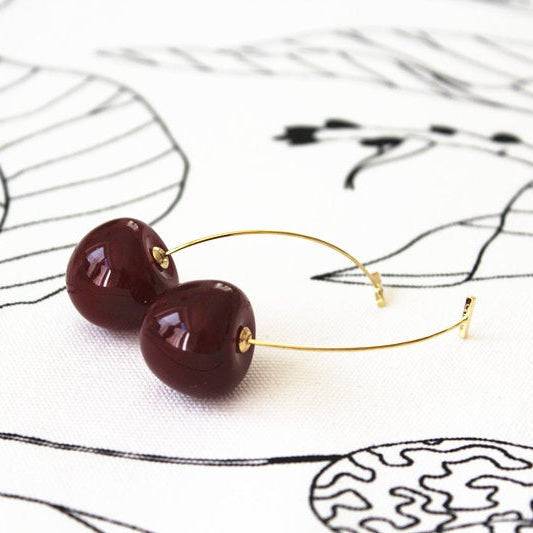 A pair of vintage rockabilly style dark red cherry earrings, featuring large resin cherries and gold-coated bronze ear wires.