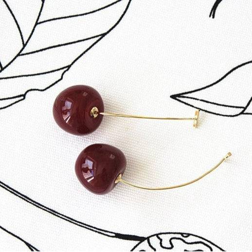 A pair of vintage rockabilly style dark red cherry earrings, featuring large resin cherries and gold-coated bronze ear wires.