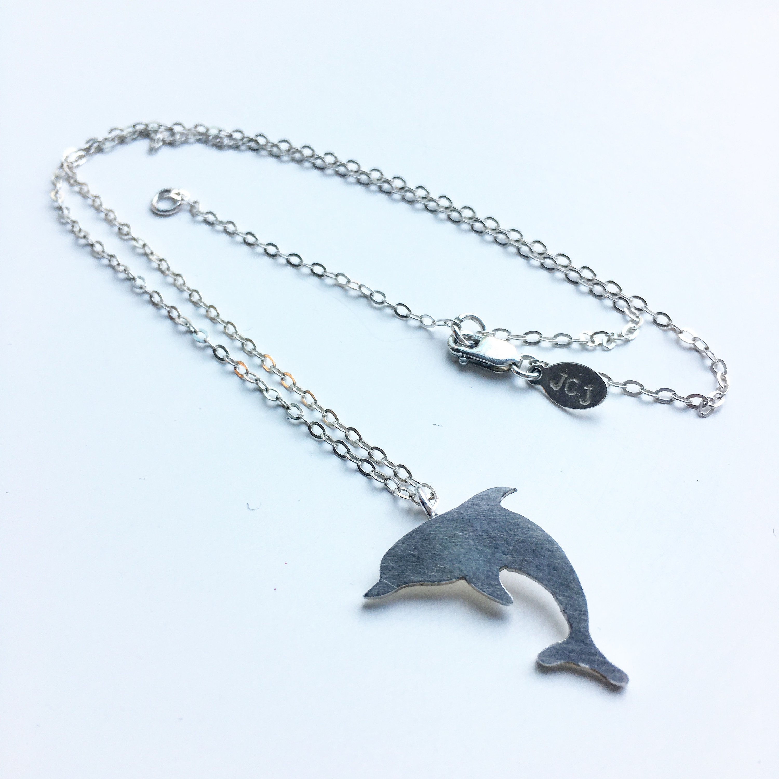 A handcrafted dolphin charm necklace made from recycled metals, featuring a whimsical design inspired by nature.