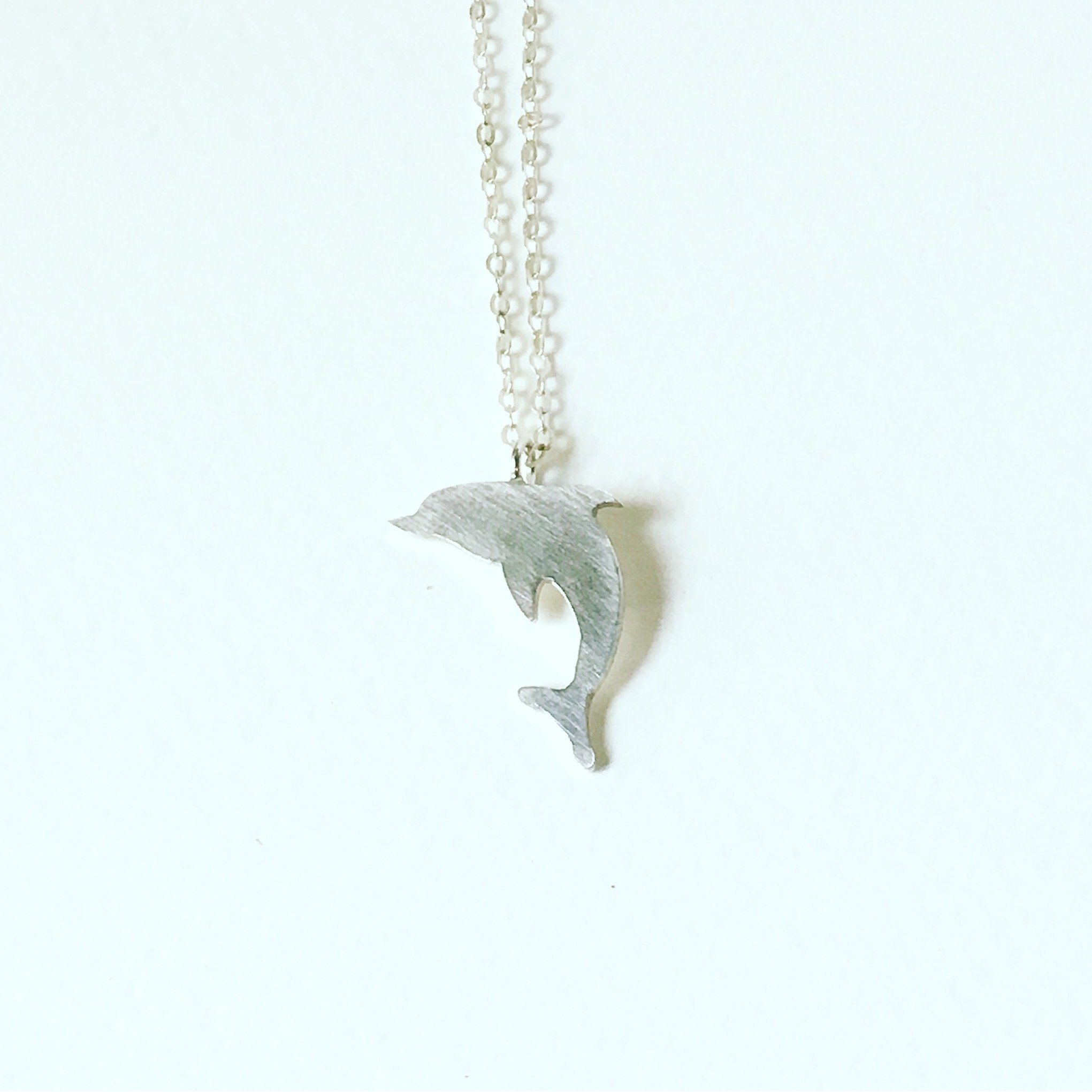 A handcrafted dolphin charm necklace made from recycled metals, featuring a whimsical design inspired by nature.