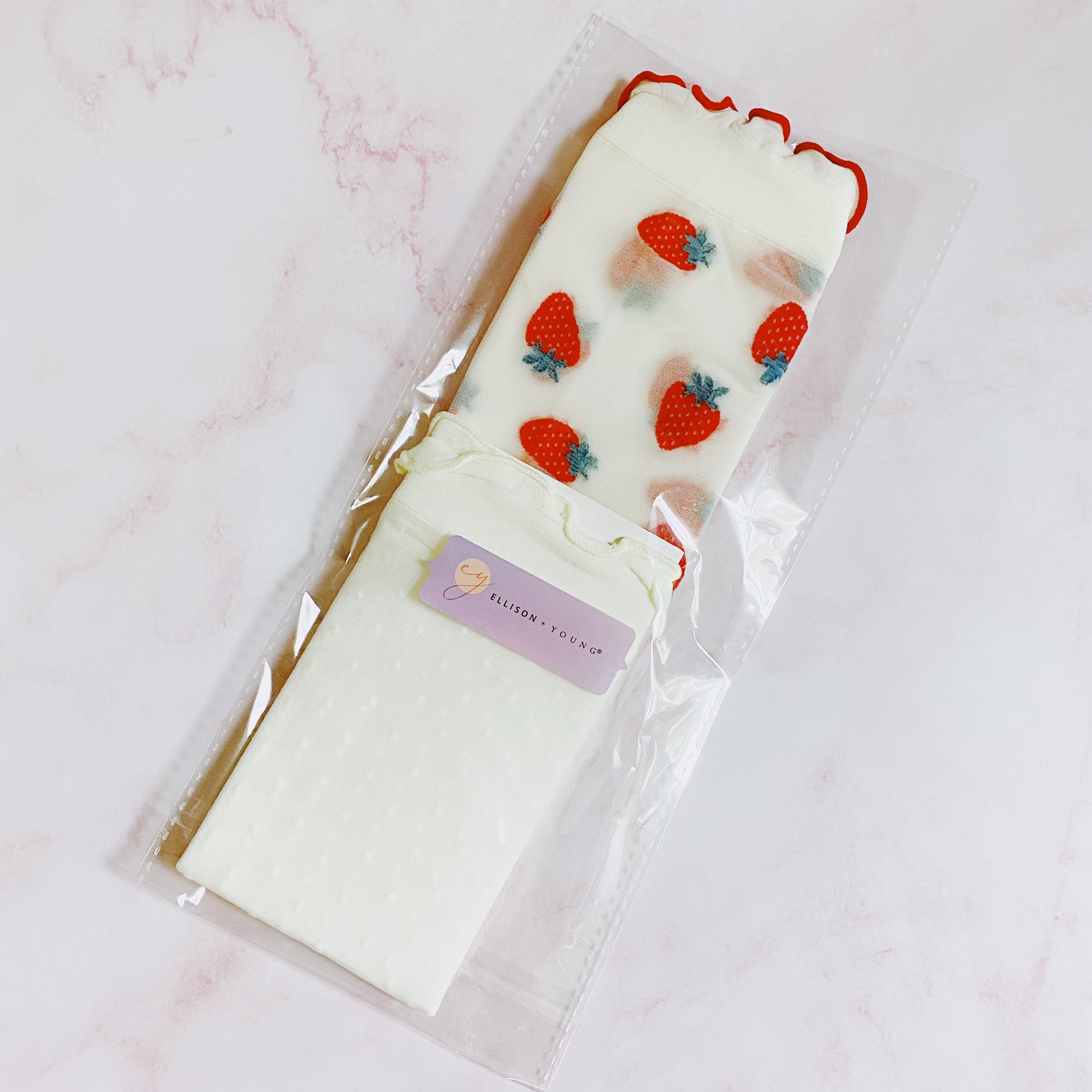 A set of two pairs of sheer socks featuring playful dots and strawberries, showcasing their soft and stretchy material.