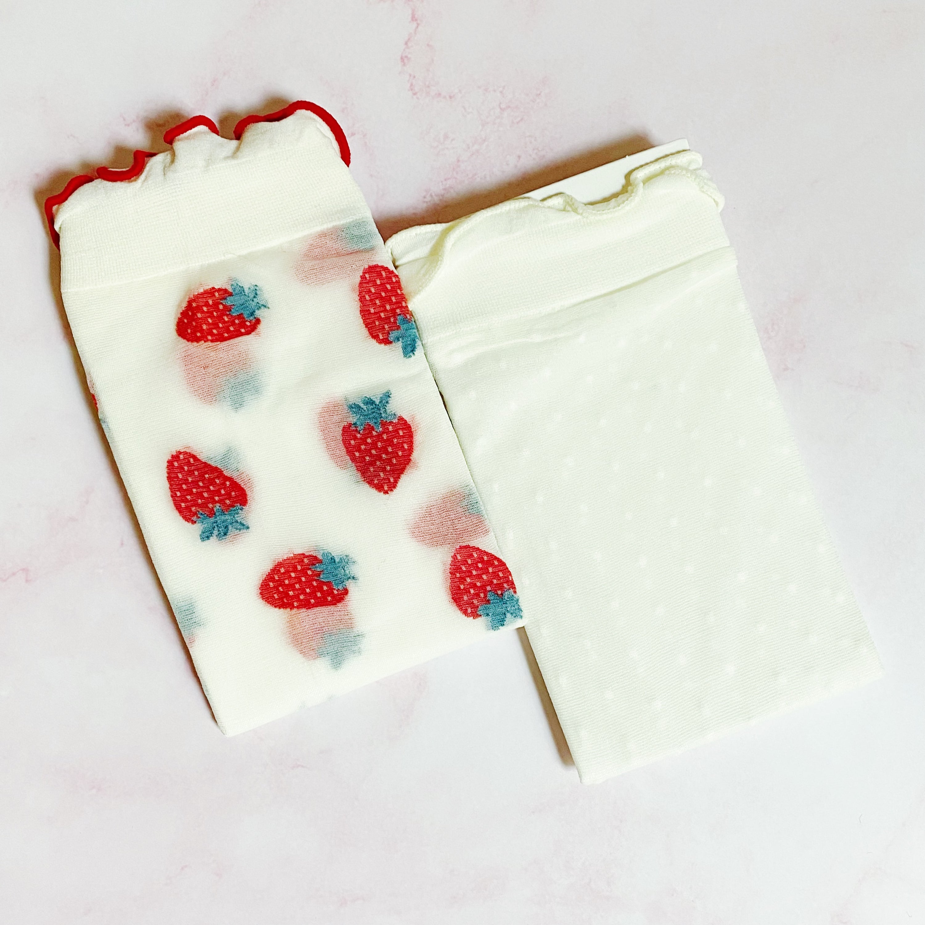 A set of two pairs of sheer socks featuring playful dots and strawberries, showcasing their soft and stretchy material.