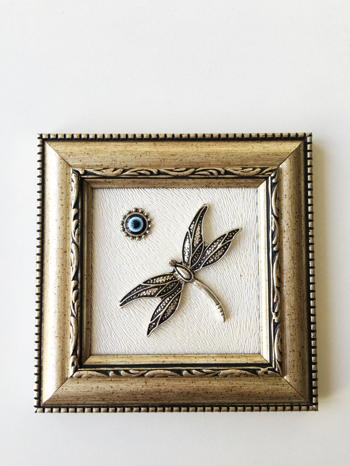 Handmade Dragonfly Framed Wall Decor featuring a silver dragonfly and a small evil eye bead, perfect for home decoration.