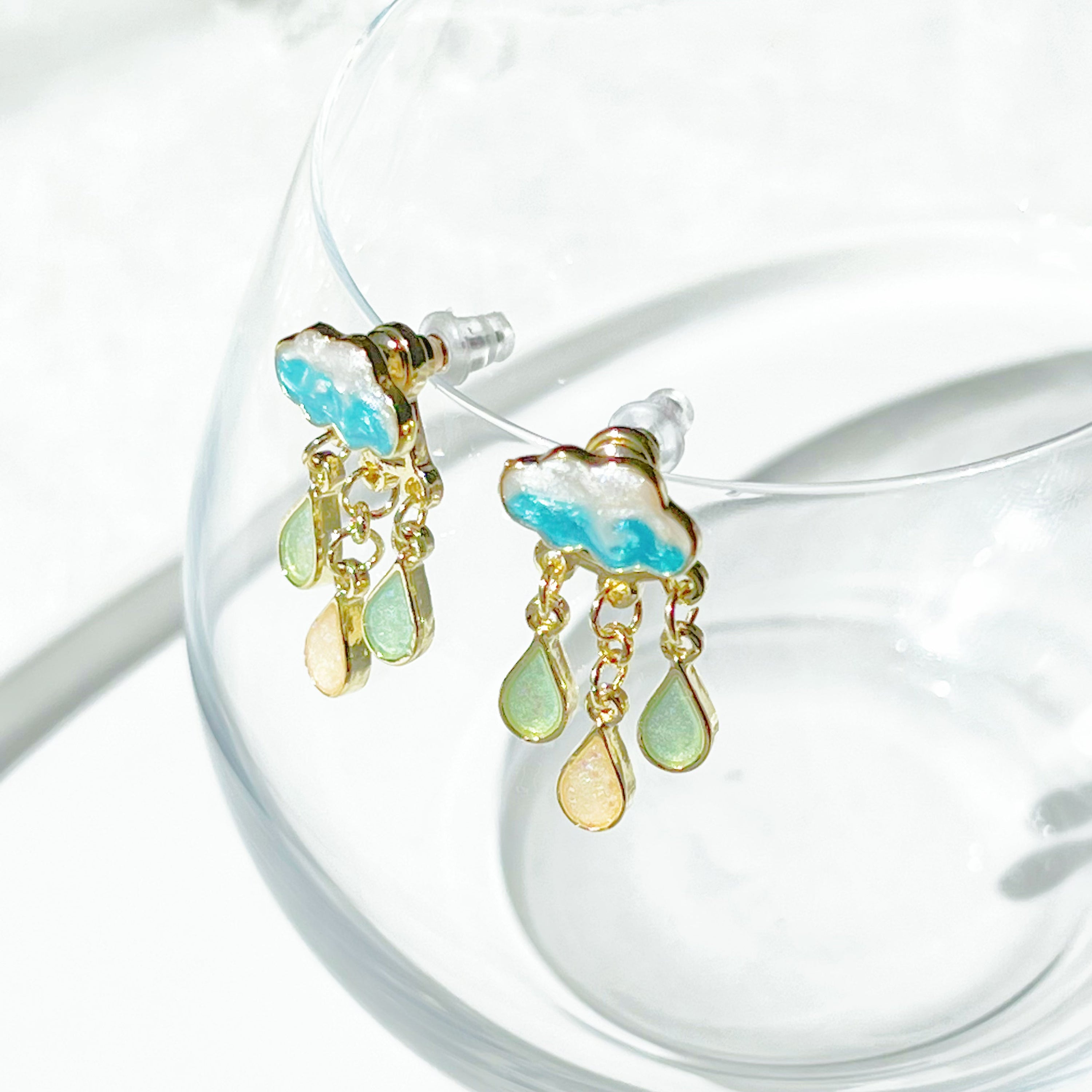 A pair of Drizzle Rain Cloud Earrings featuring sterling silver ear studs and gold plated bronze clouds, symbolizing positivity.