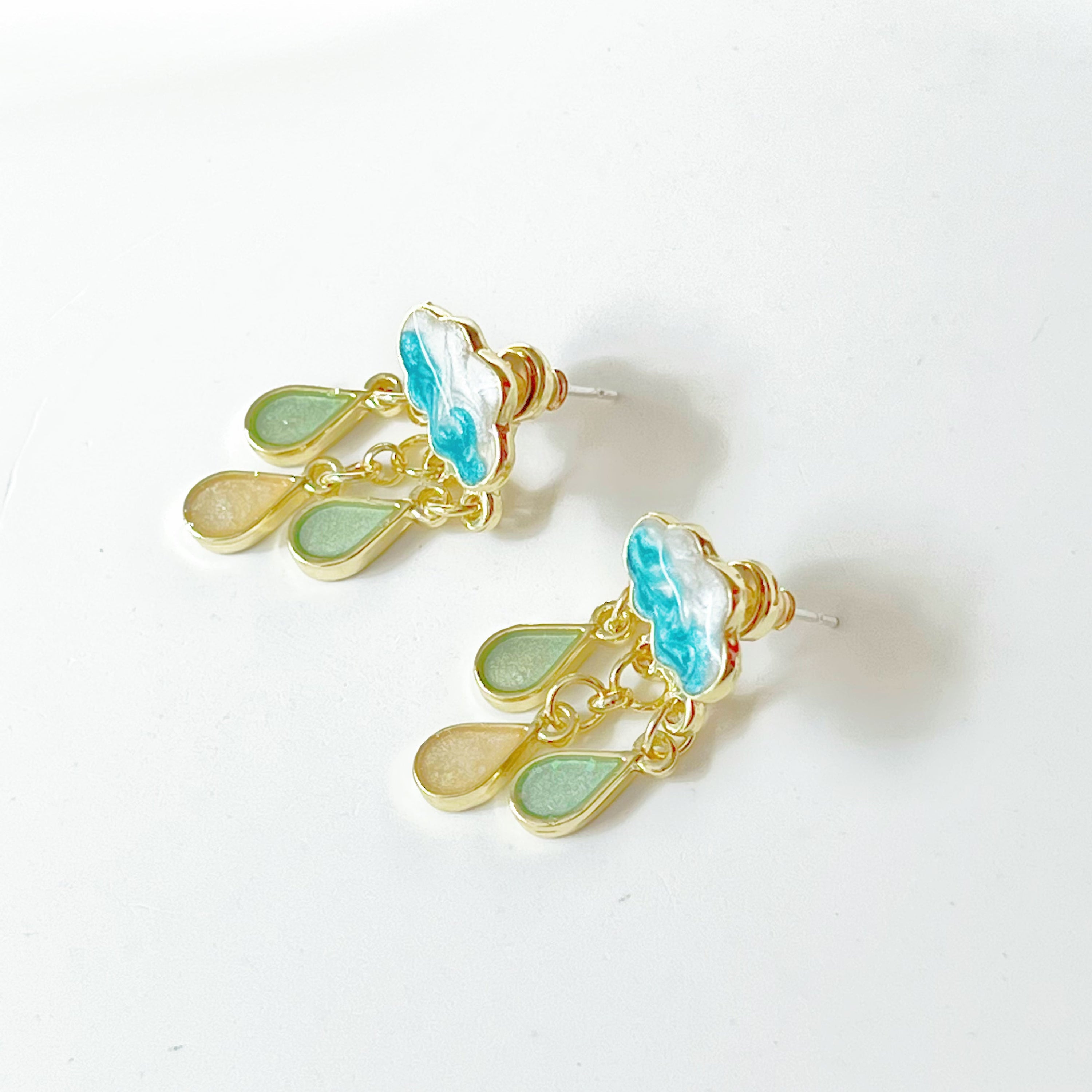 A pair of Drizzle Rain Cloud Earrings featuring sterling silver ear studs and gold plated bronze clouds, symbolizing positivity.