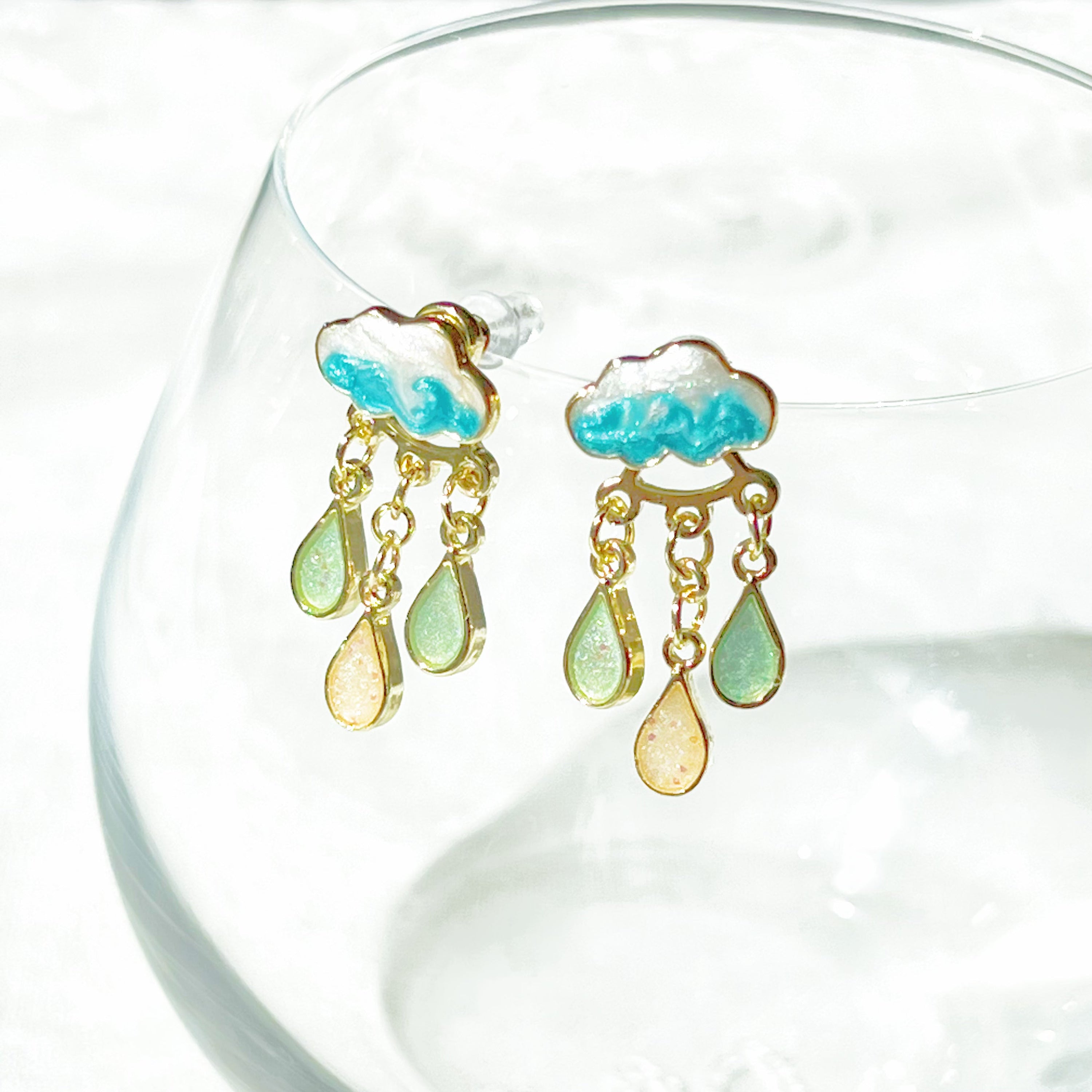 A pair of Drizzle Rain Cloud Earrings featuring sterling silver ear studs and gold plated bronze clouds, symbolizing positivity.