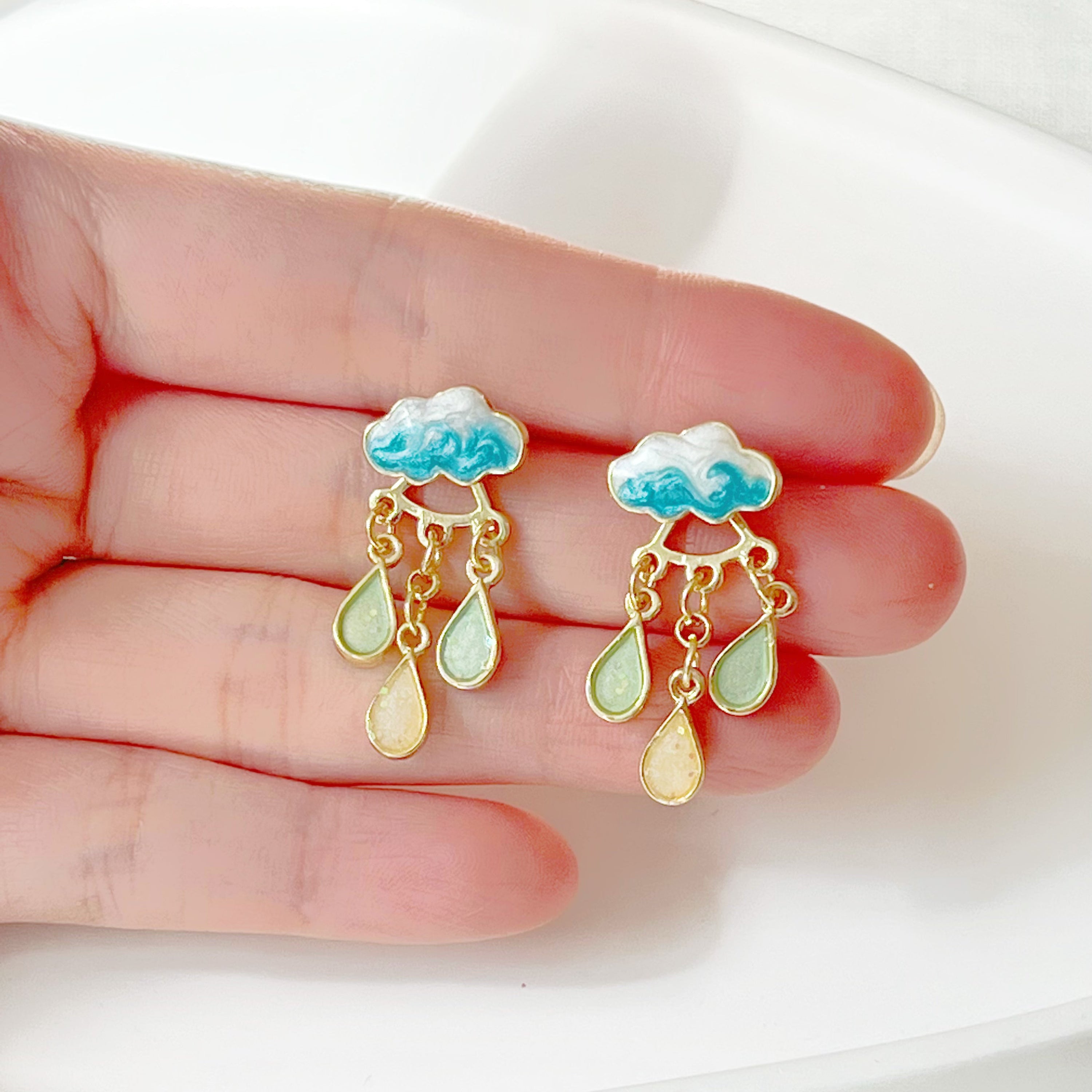 A pair of Drizzle Rain Cloud Earrings featuring sterling silver ear studs and gold plated bronze clouds, symbolizing positivity.