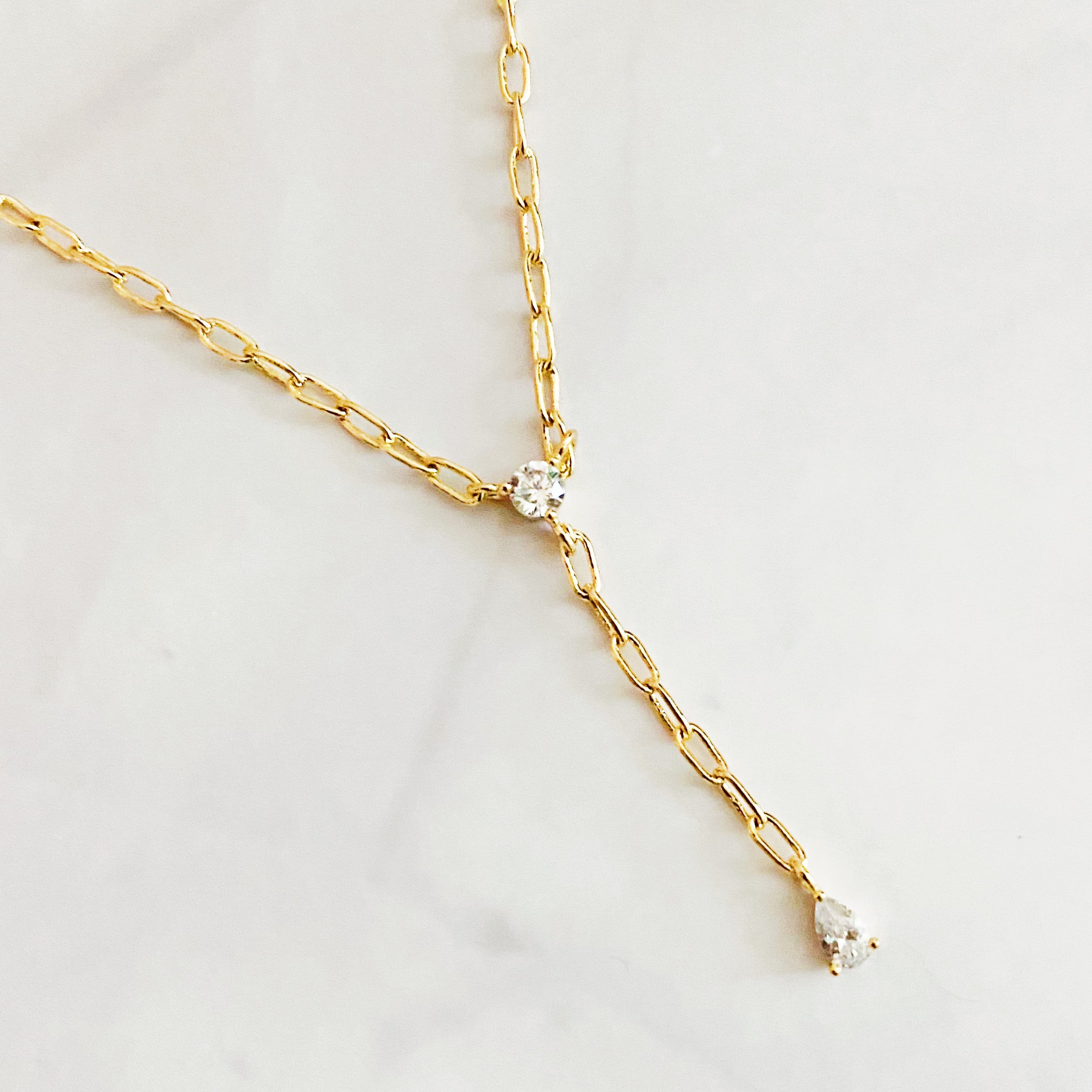 A delicate gold plated brass necklace featuring a T drop design with sparkling cubic zirconia stones, elegantly displayed on a soft background.