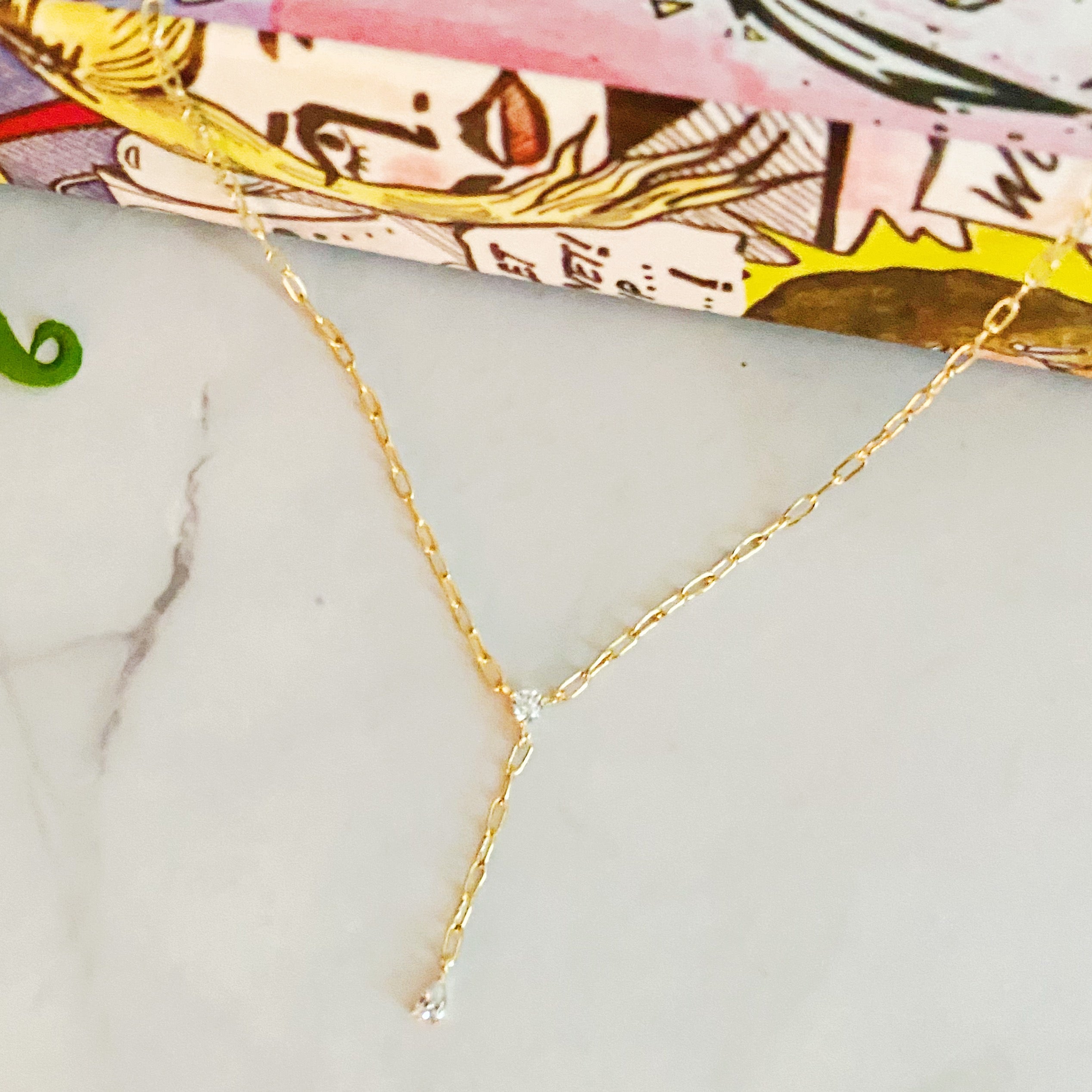 A delicate gold plated brass necklace featuring a T drop design with sparkling cubic zirconia stones, elegantly displayed on a soft background.