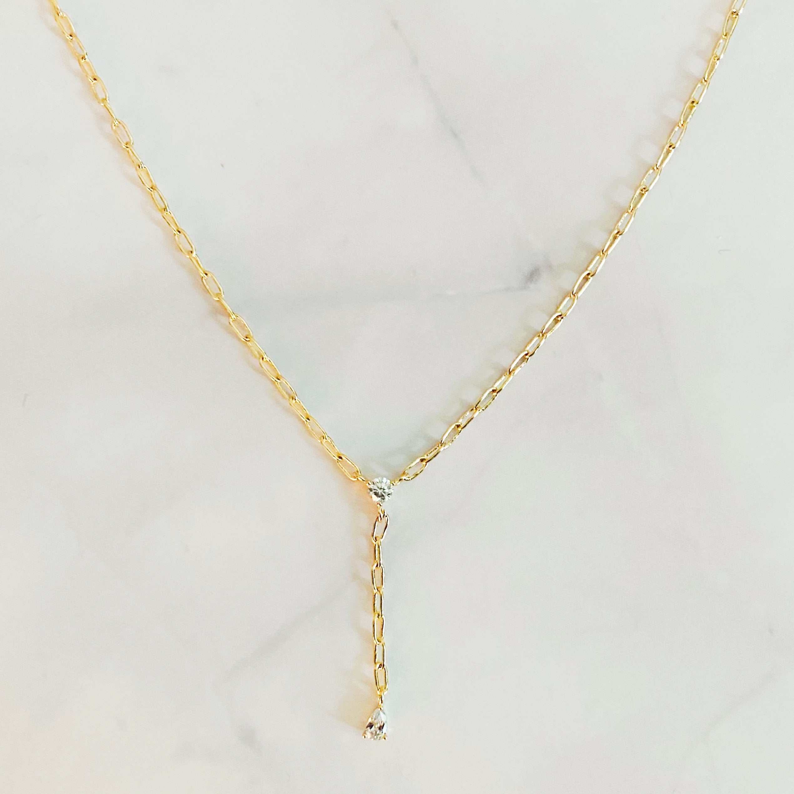 A delicate gold plated brass necklace featuring a T drop design with sparkling cubic zirconia stones, elegantly displayed on a soft background.