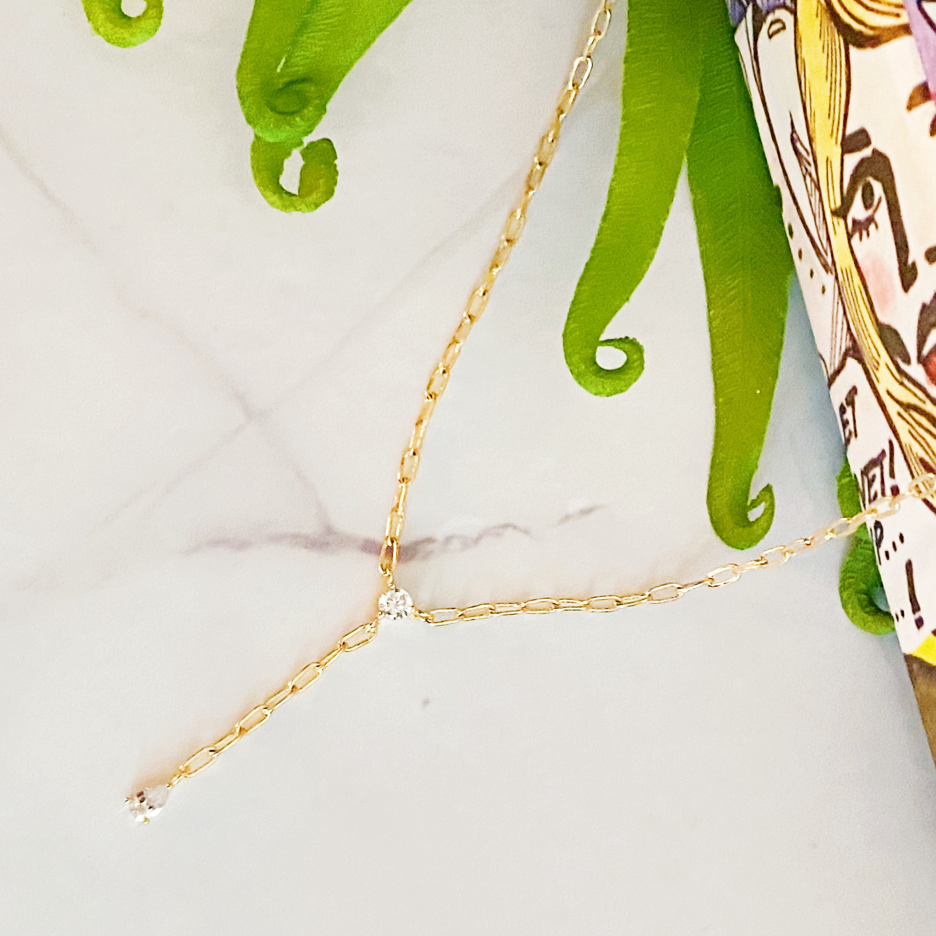 A delicate gold plated brass necklace featuring a T drop design with sparkling cubic zirconia stones, elegantly displayed on a soft background.