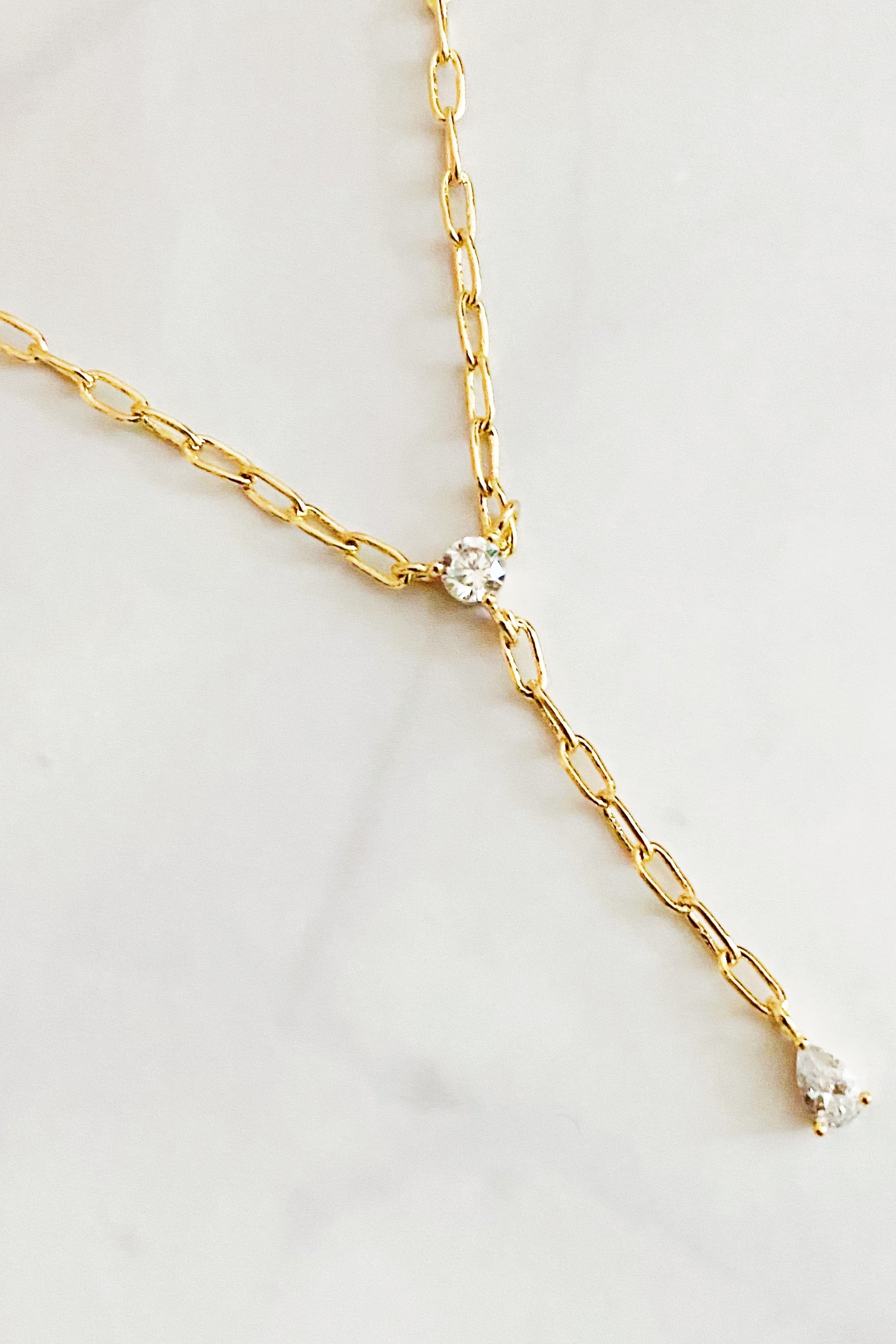 A delicate gold plated brass necklace featuring a T drop design with sparkling cubic zirconia stones, elegantly displayed on a soft background.