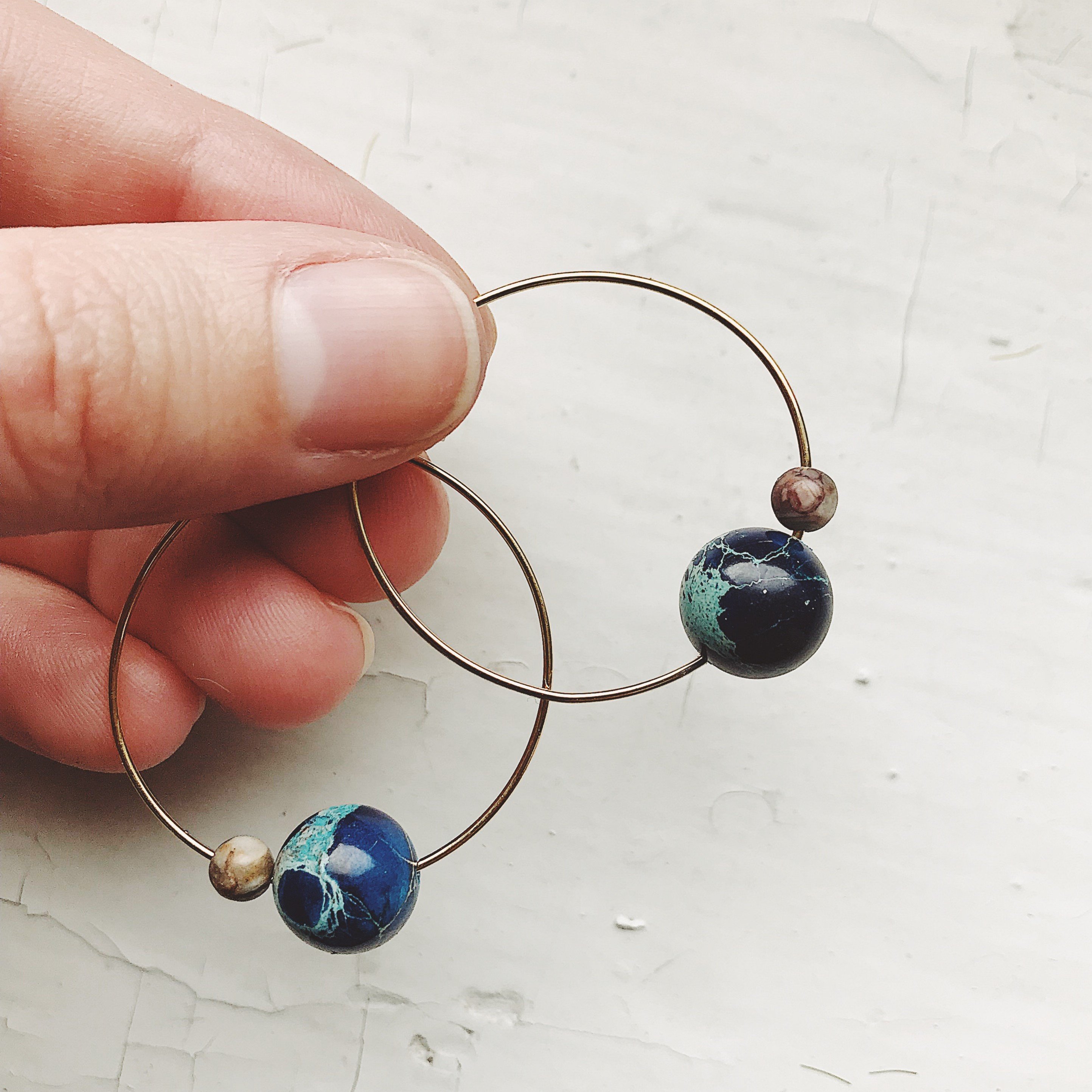 A pair of Earth and Moon Jasper Bead Hoop Earrings featuring colorful jasper beads on a raw brass hoop, showcasing a cosmic design.